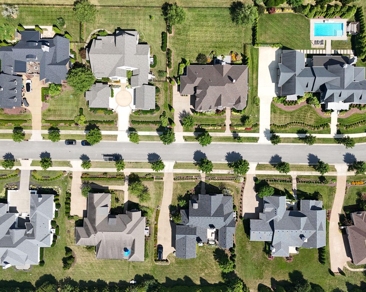 Overhead shot of homes in a suburban neighborhood, showcasing lush greenery.