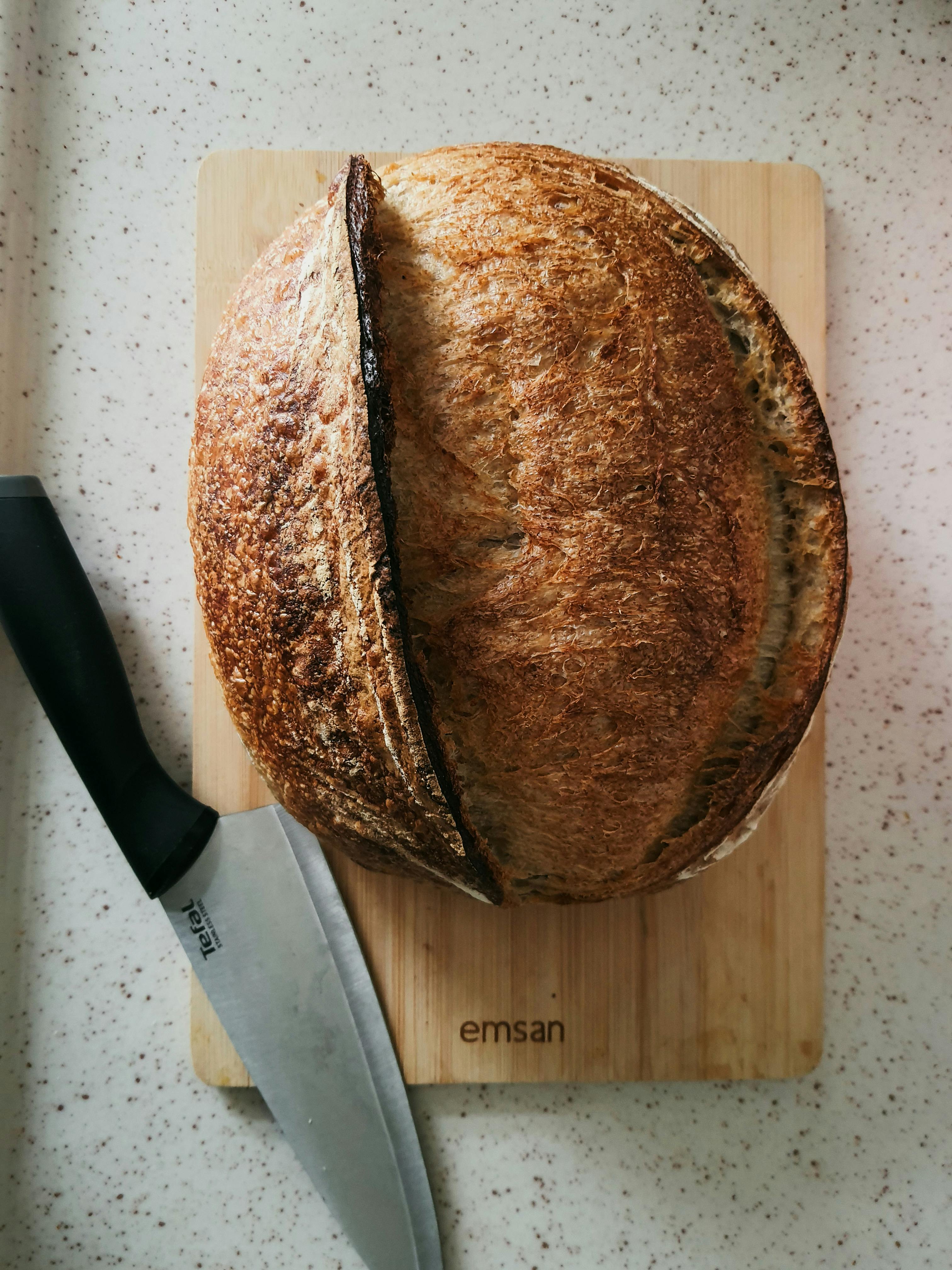 A round loaf of sourdough bread on a wooden cutting board with a knife, ideal for culinary imagery.