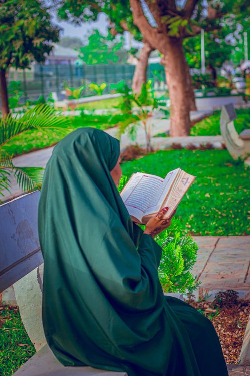 Free Woman in traditional attire reading in a serene outdoor park setting, surrounded by greenery. Stock Photo