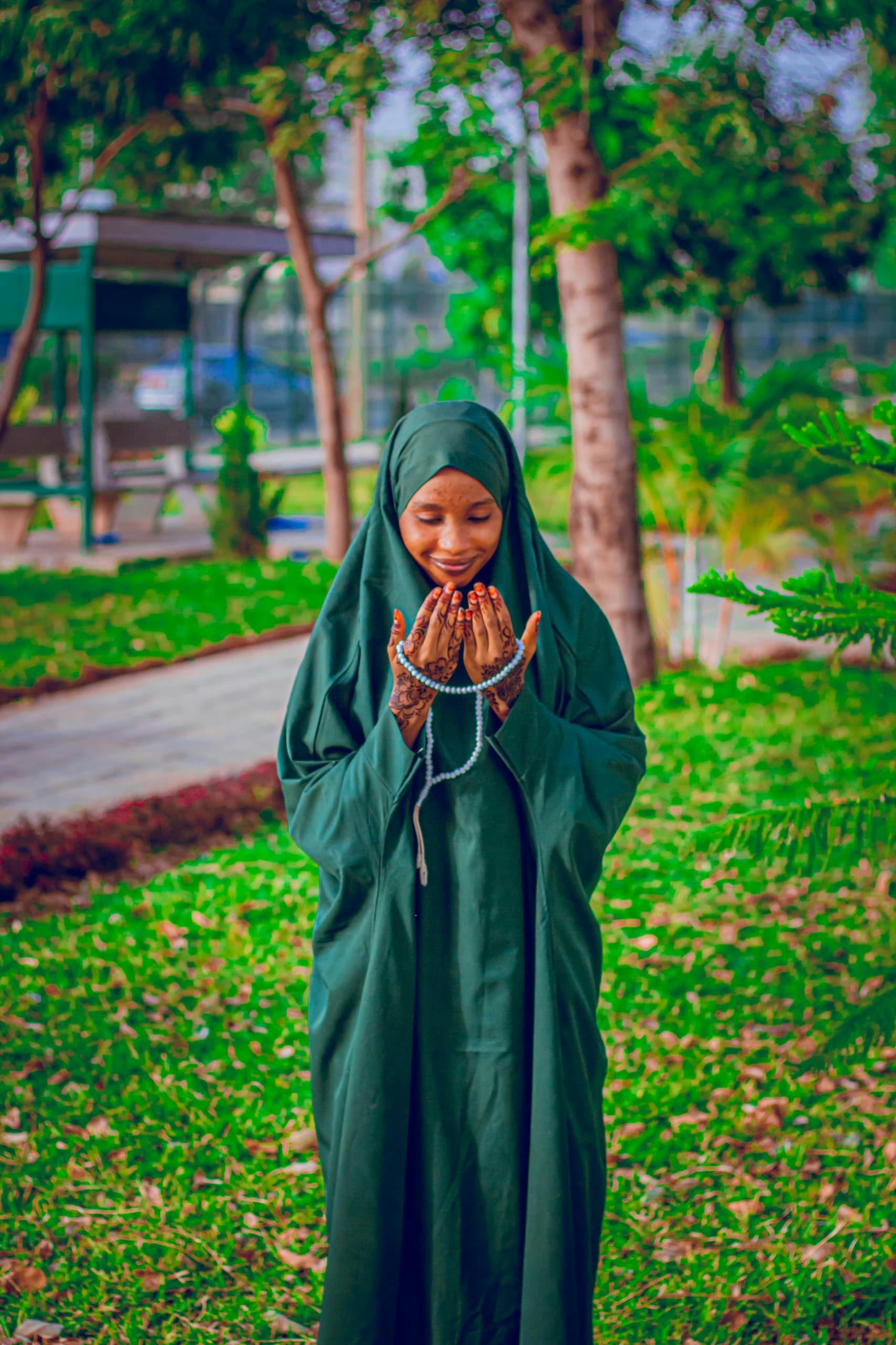 Gratis Giovane donna con hijab verde che prega con il rosario in un parco. Foto a disposizione