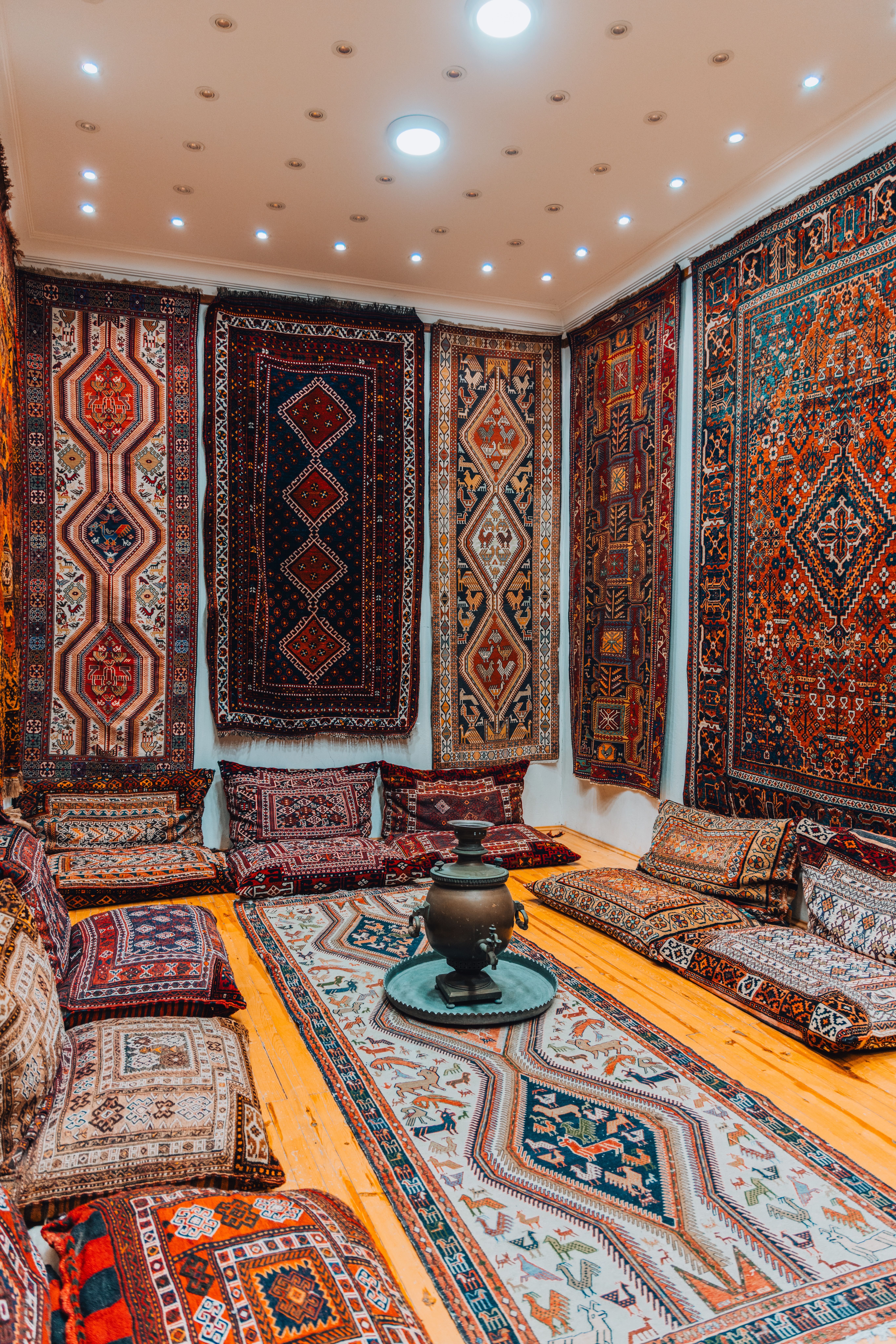 Banquettes de coussins tissés posées au sol, tapis de laine suspendus aux murs et samovar de cuivre