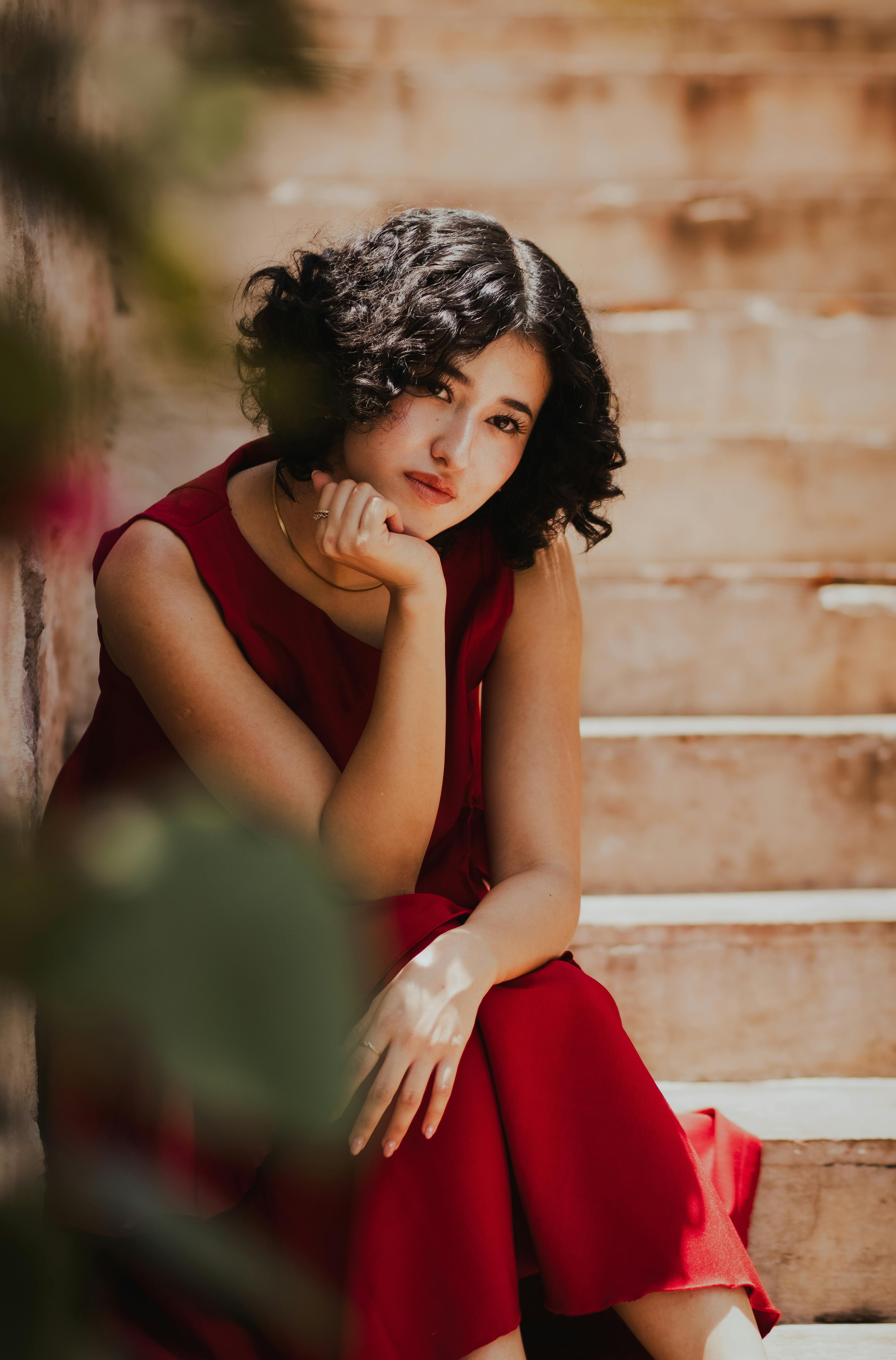 Gratis Donna elegantemente vestita, seduta su gradini di pietra in una posa pensierosa, ambiente luminoso e caldo. Foto a disposizione