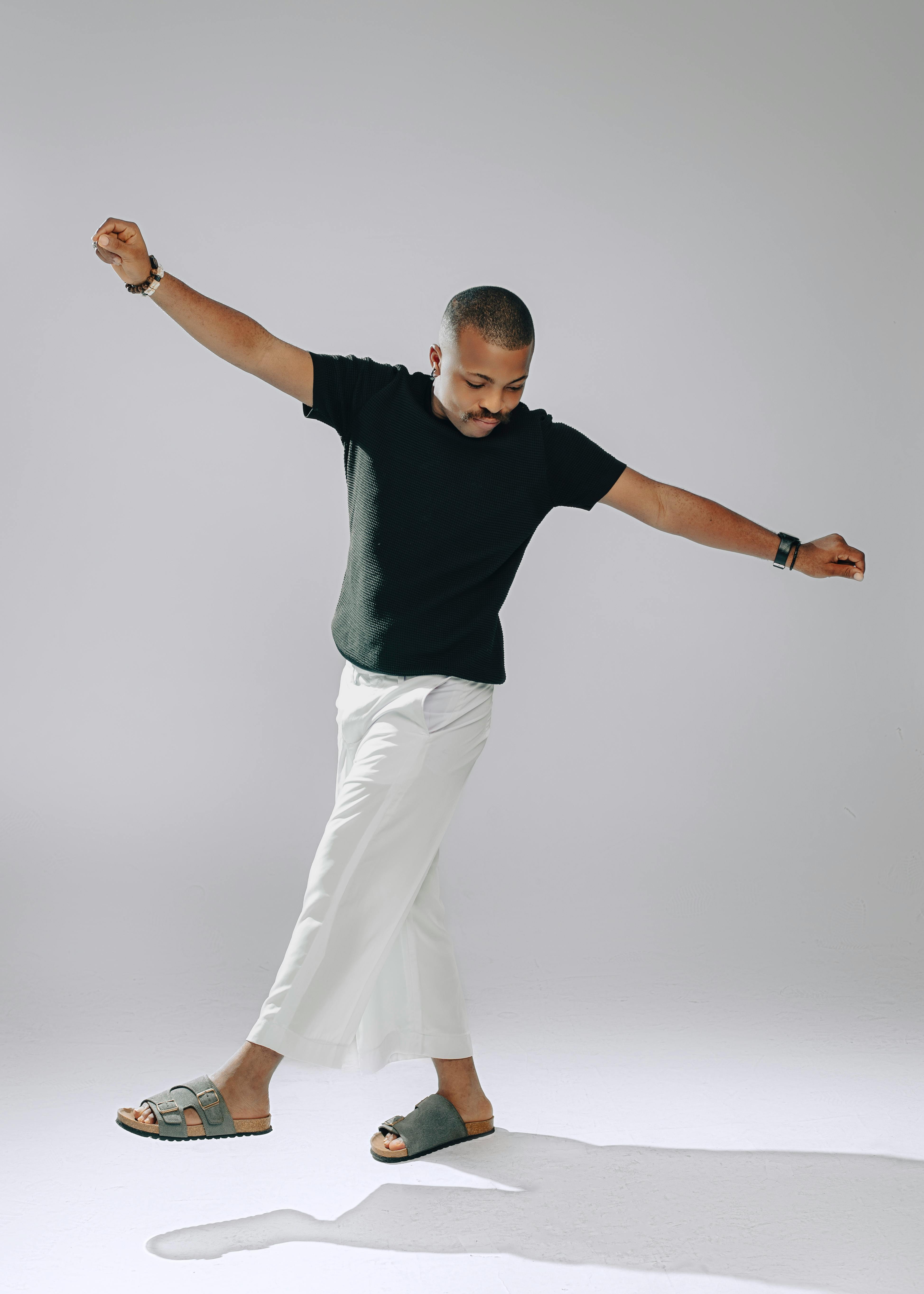 bezplatná Ležérní muž v bílých kalhotách a černé košili pózuje s nataženýma rukama uvnitř. Základová fotografie