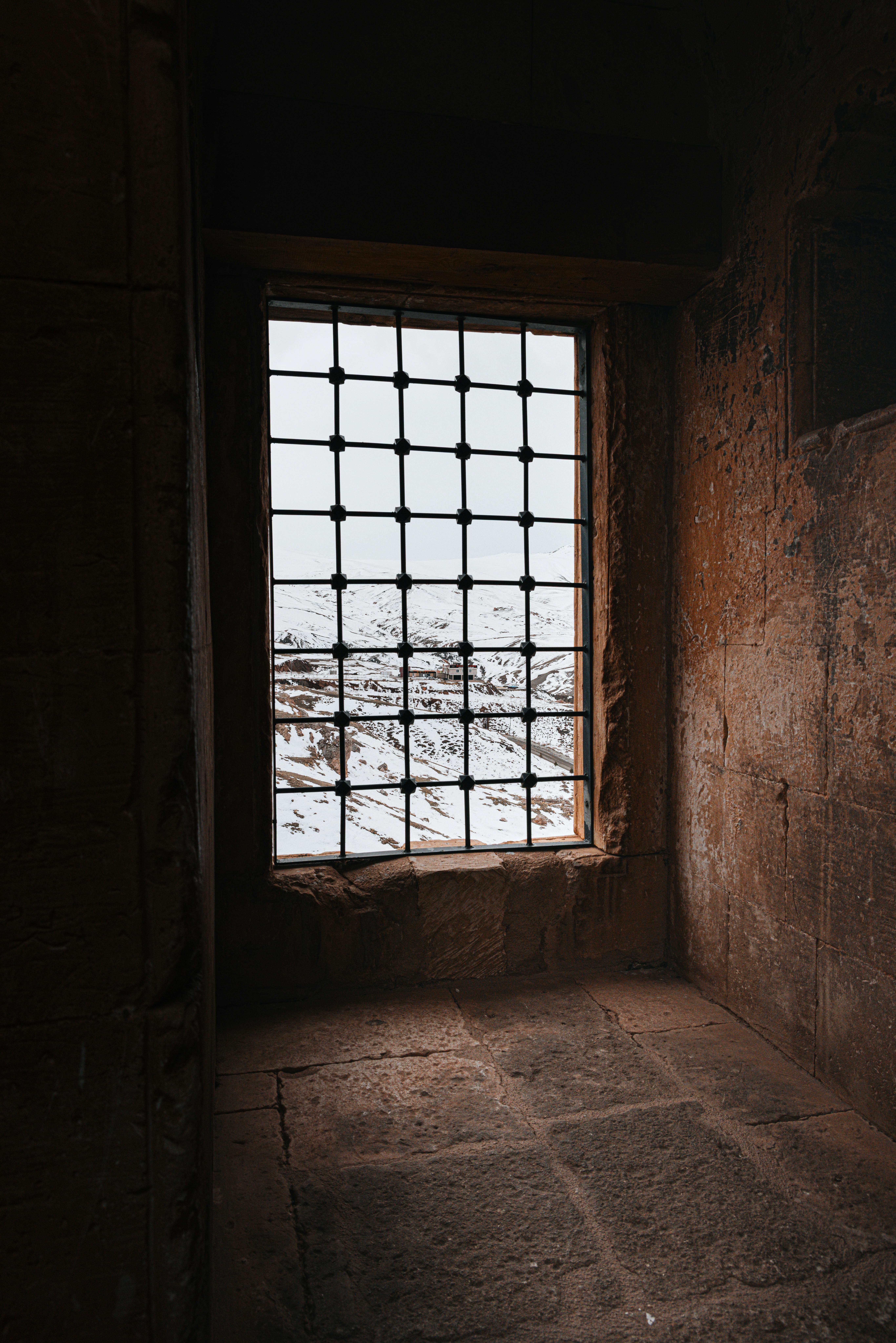 Kostenlos Ein Fenster im gotischen Stil mit Blick auf eine verschneite Landschaft in Ağrı, Türkei, das Kontrast und Textur zur Schau stellt. Stock-Foto
