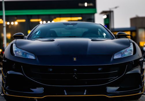 Front view of a luxurious black sports car at an urban location with blurred city lights.