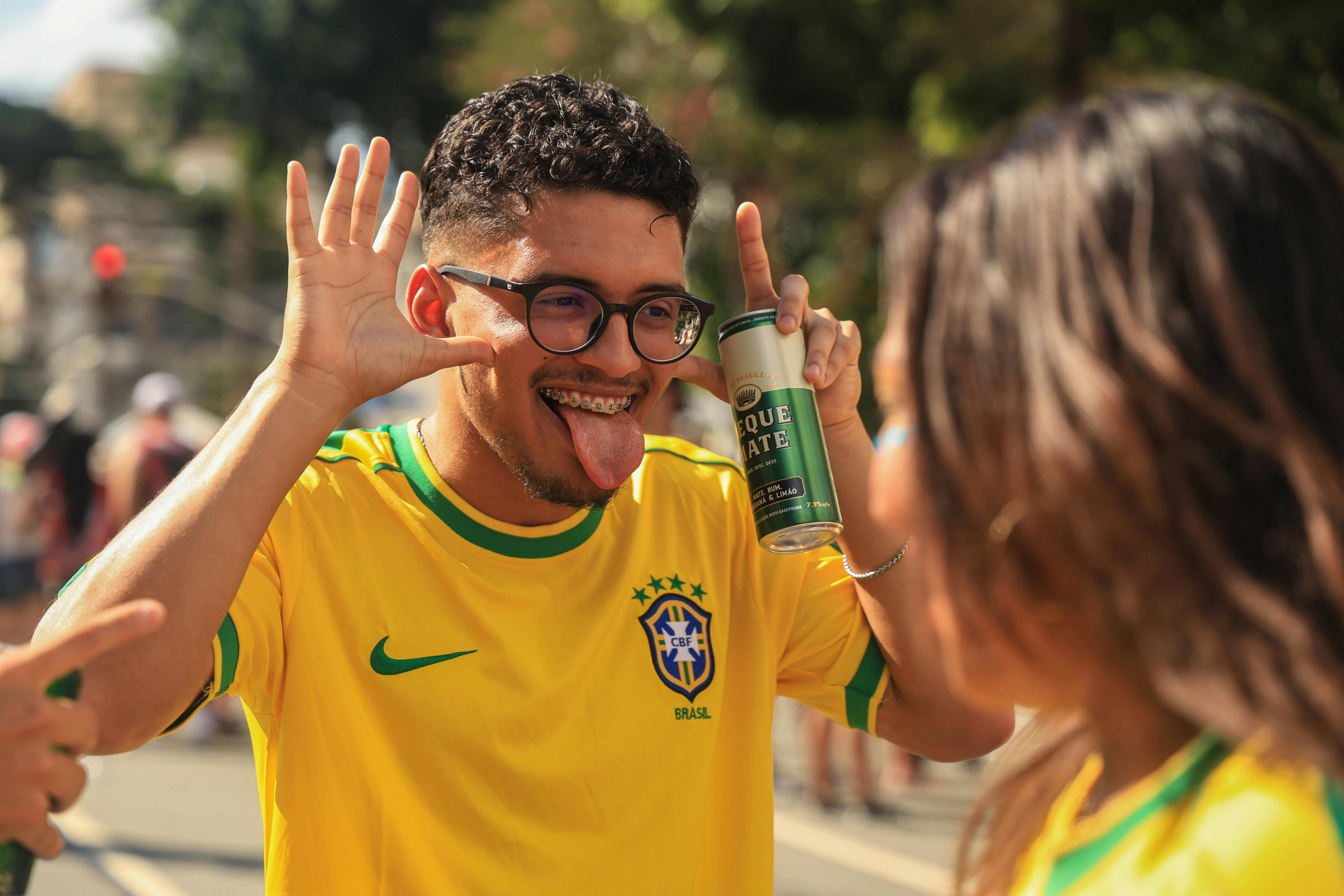 bezplatná Šťastný brazilský fotbalový fanoušek ve žlutém dresu dělá hravá gesta během živé venkovní akce. Základová fotografie