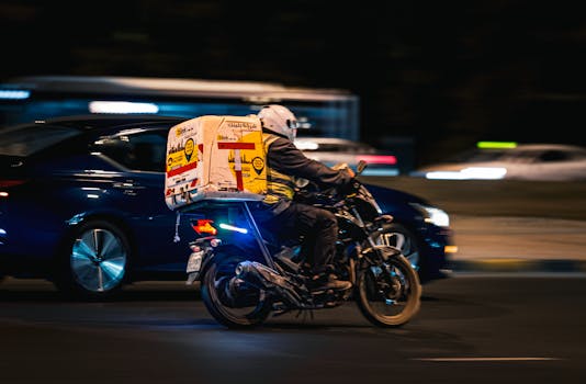 A delivery motorbike speeds through the streets of Kuwait City at night, showcasing fast-paced urban life.