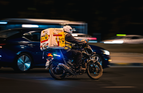 Free A delivery motorbike speeds through the streets of Kuwait City at night, showcasing fast-paced urban life. Stock Photo