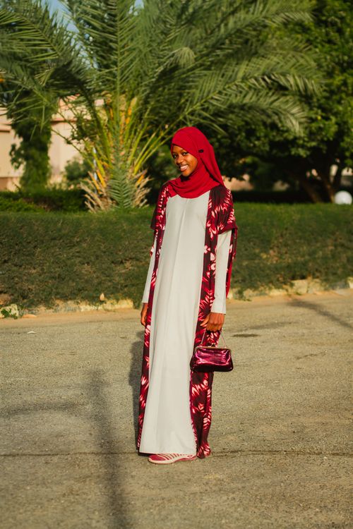 Free A woman in a red hijab and floral garment stands confidently outdoors, showcasing elegant traditional fashion. Stock Photo