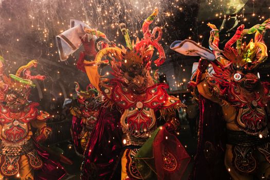 Colorful Bolivian carnival dancers in traditional costumes with sparklers and fireworks at night.