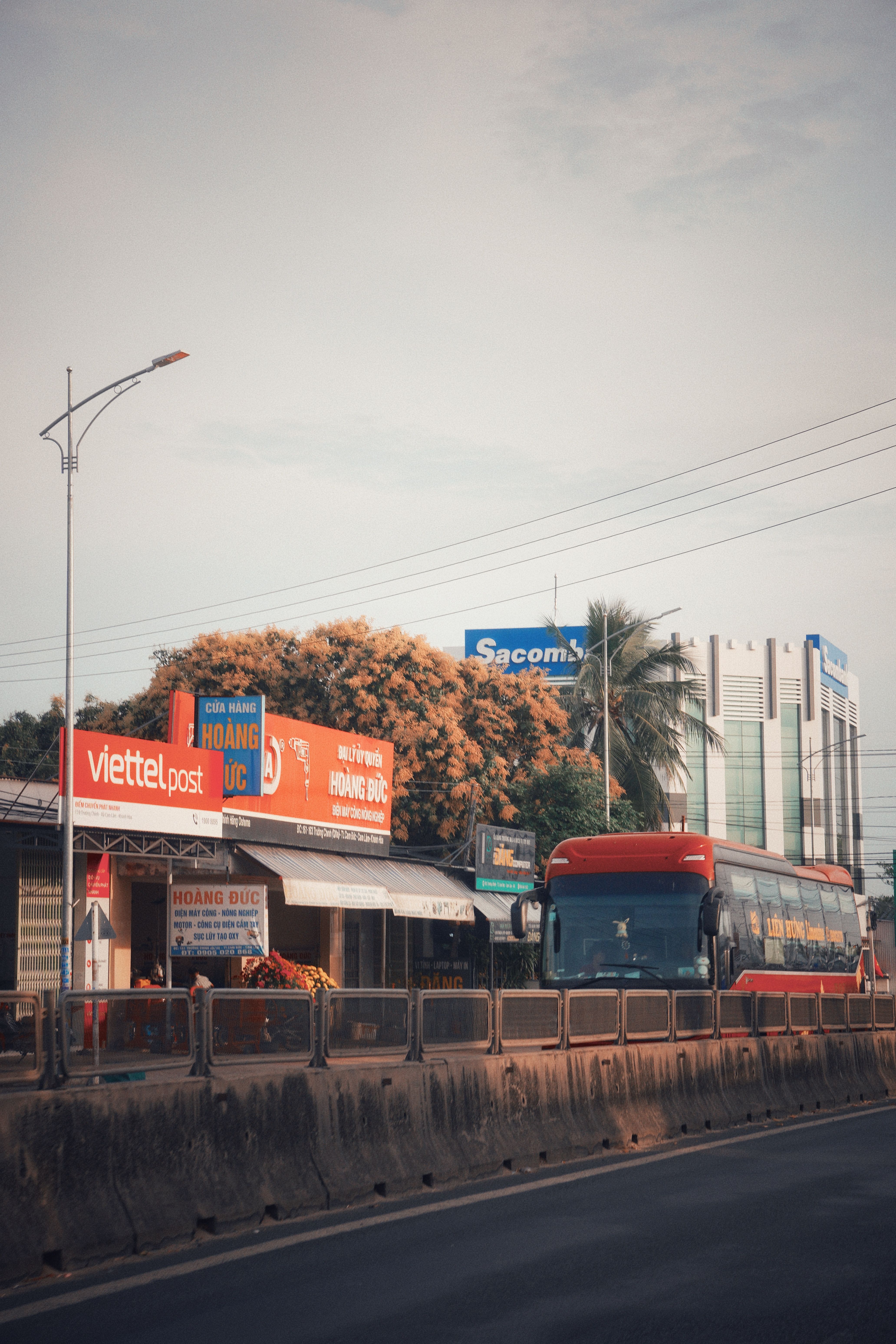 Street scene in Vietnam featuring a red bus, retail signage, and modern buildings in a lively urban setting.