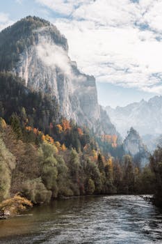 Serene autumn landscape with misty mountains, vibrant foliage, and tranquil river.