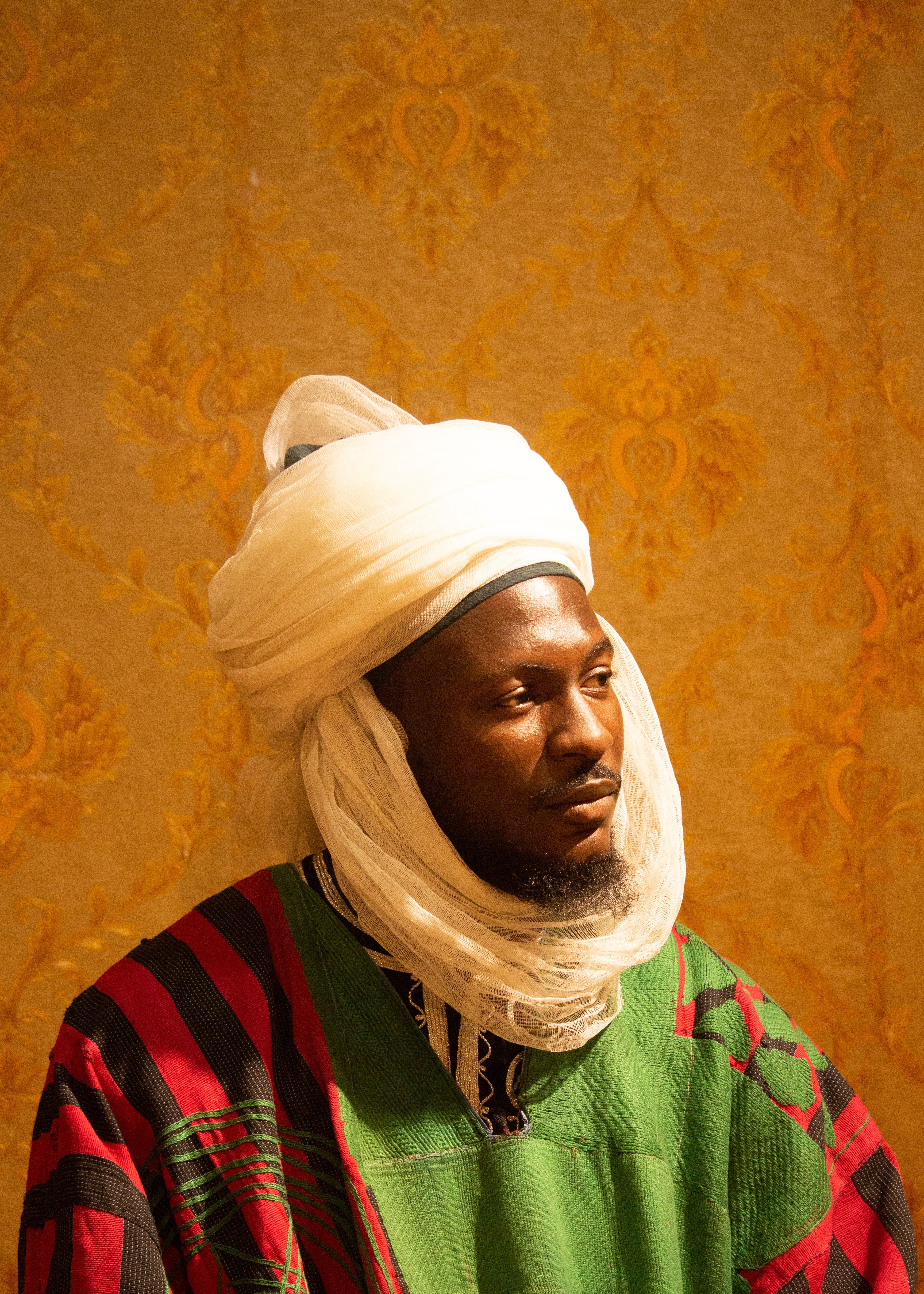A man in colorful traditional attire poses against a detailed golden background.