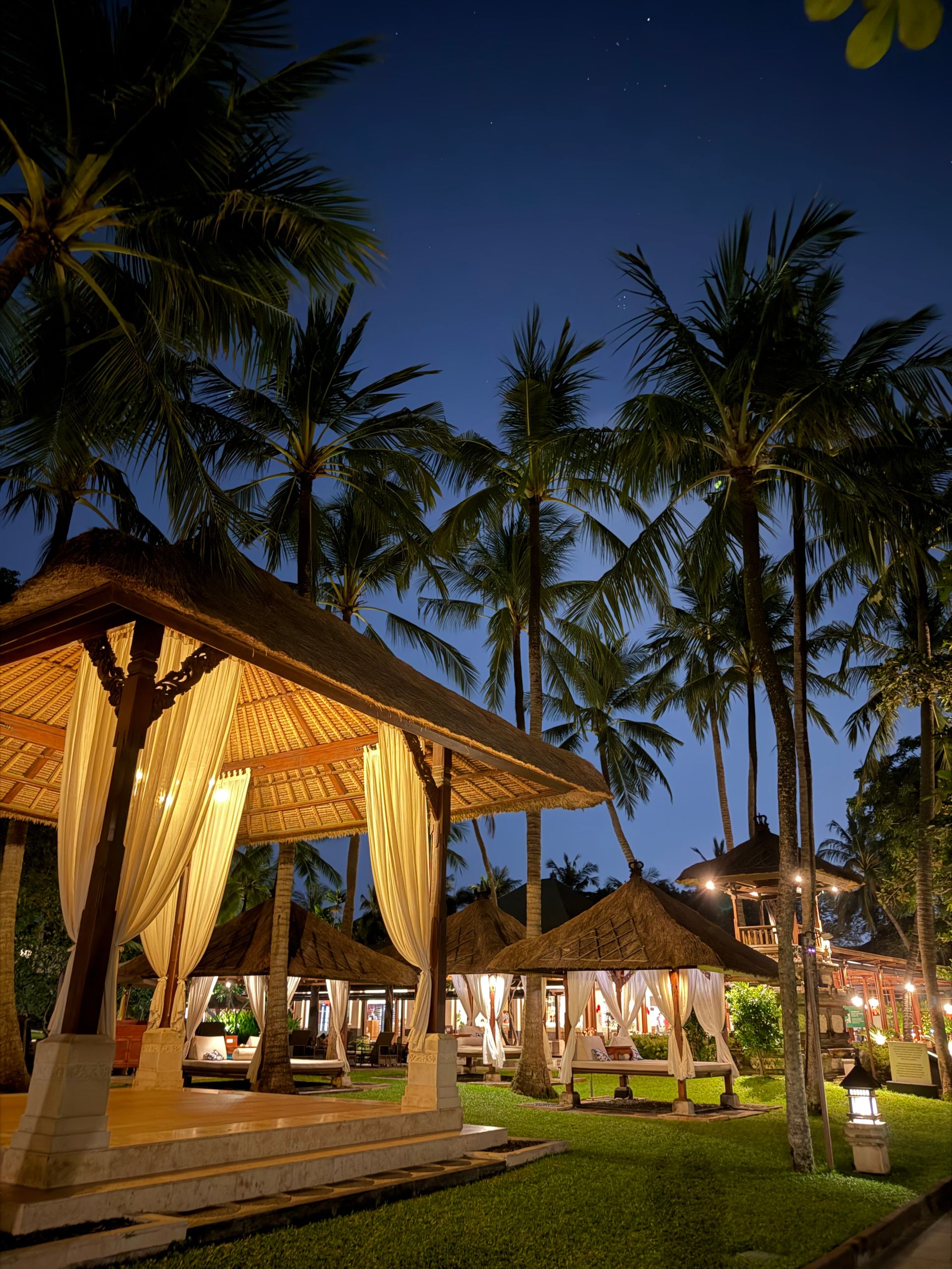 Peaceful tropical night scene at a Balinese resort with illuminated gazebos and palm trees.