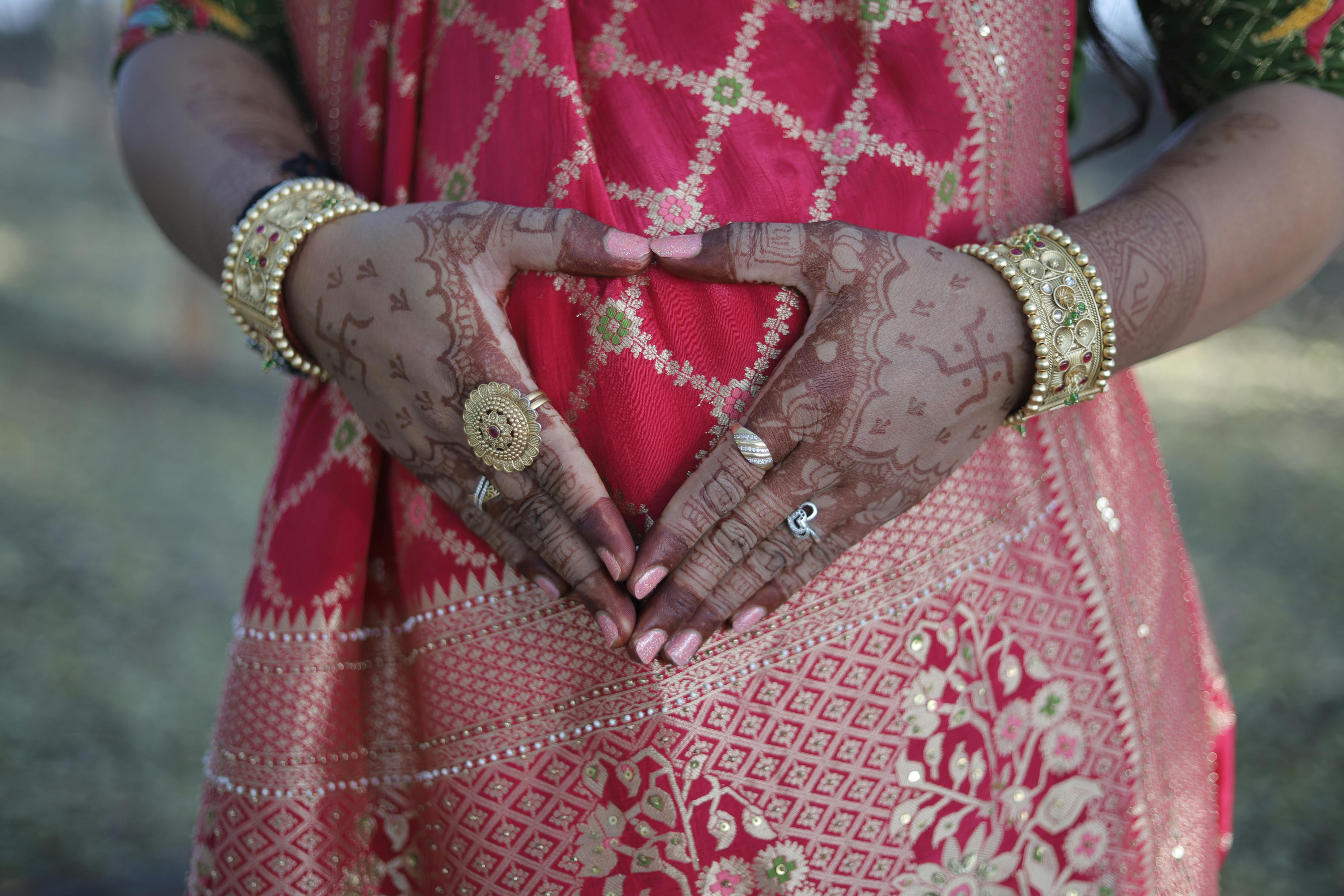 Gratis Una donna in abiti tradizionali forma un cuore con le mani decorate con l'henné all'aperto. Foto a disposizione