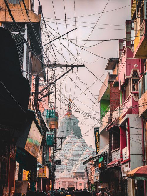 Free A busy alleyway leading to a magnificent temple, framed by vibrant buildings and power lines. Stock Photo