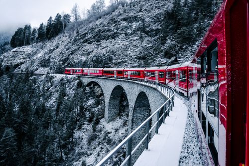Free Scenic view of a red train on a snow-covered bridge in the Swiss Alps, showcasing winter beauty. Stock Photo