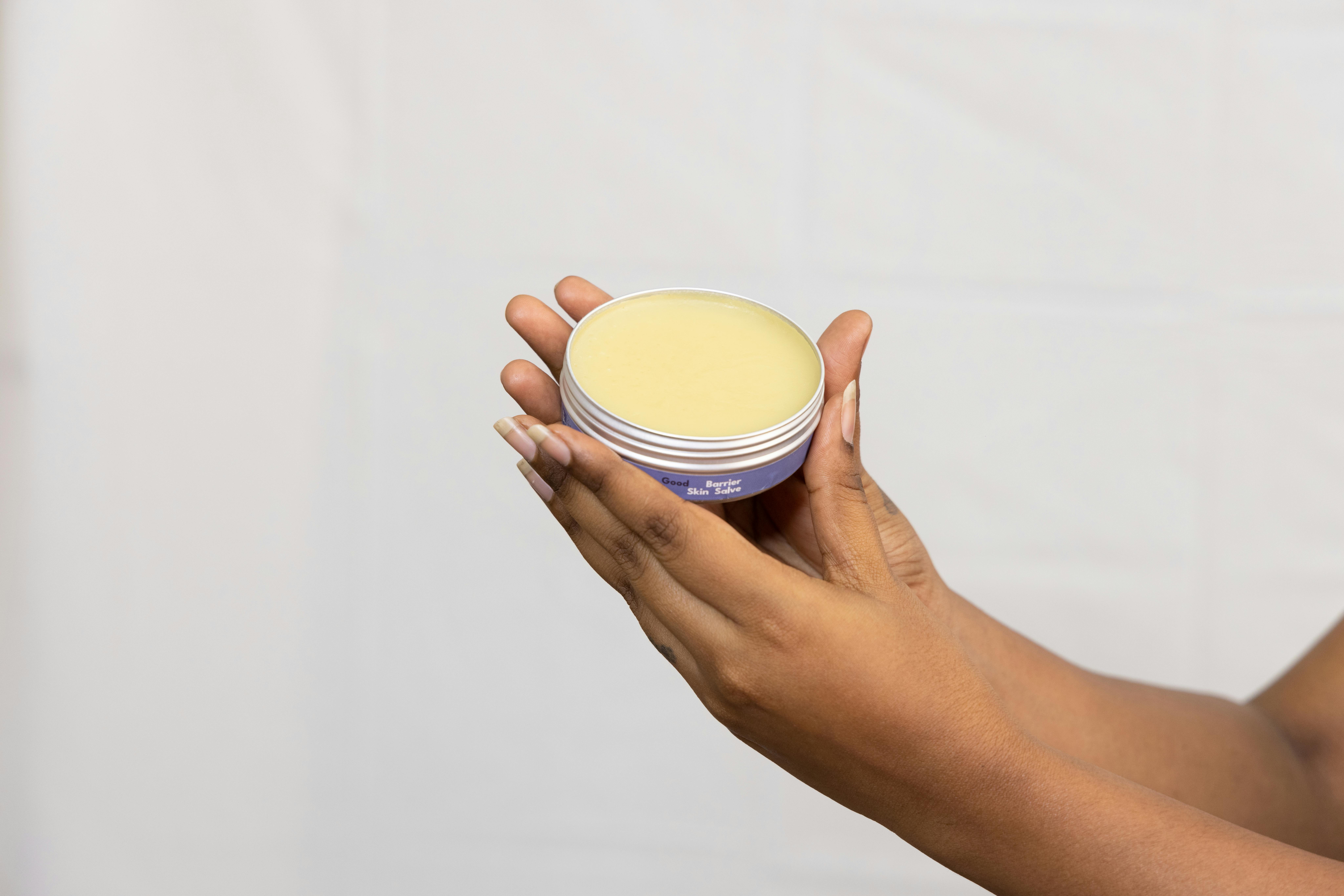 A close-up of hands holding a jar of moisturizing cream against a neutral backdrop, emphasizing skincare.