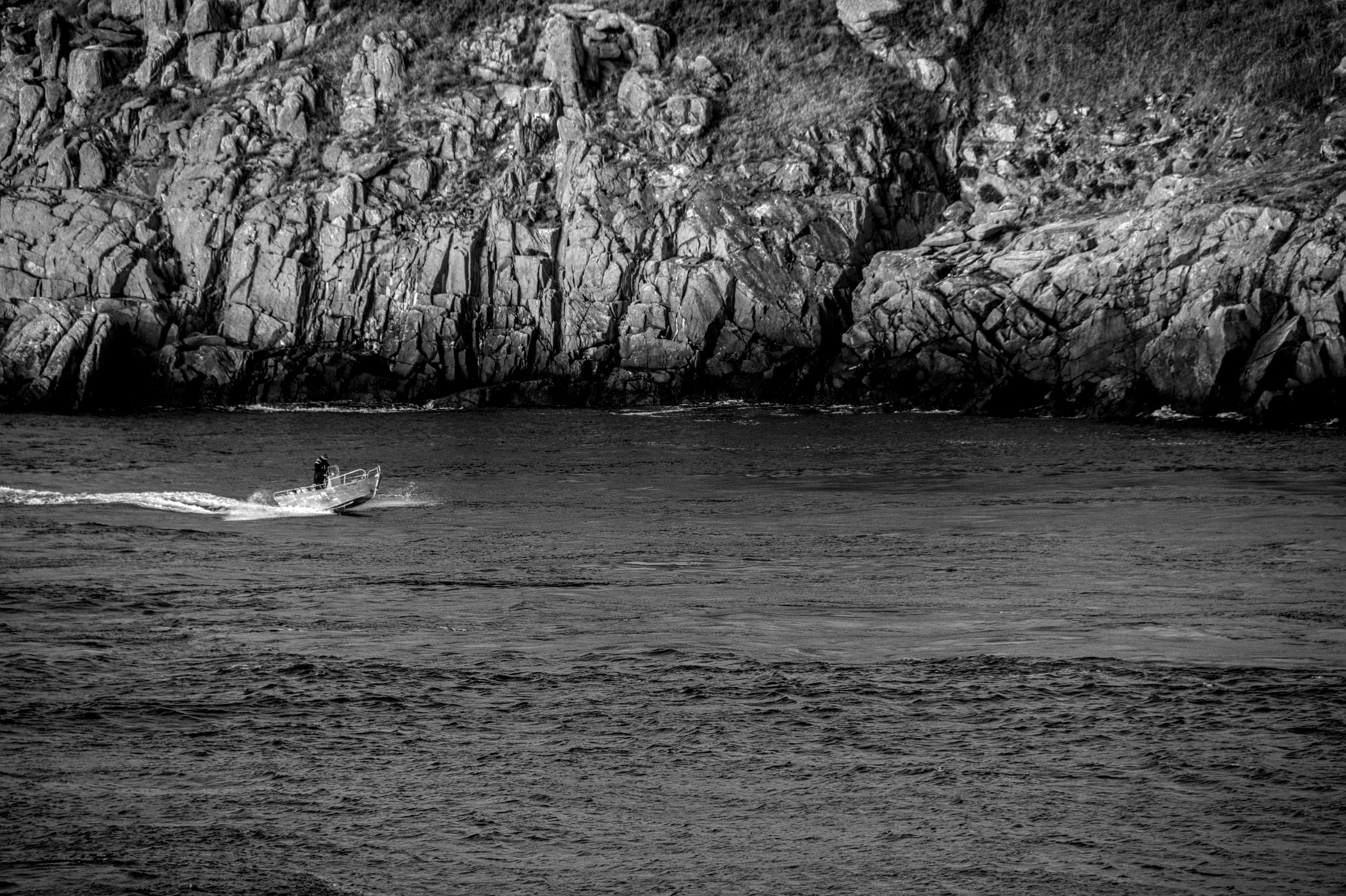 Ilmainen Pieni vene navigoi karujen rannikkokallioiden lähellä Bretagnessa, Ranskassa. Kuvapankkikuva