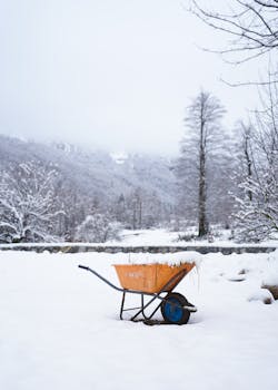 A lone wheelbarrow covered in snow amidst the serene winter landscape of Valbonë, Albania.