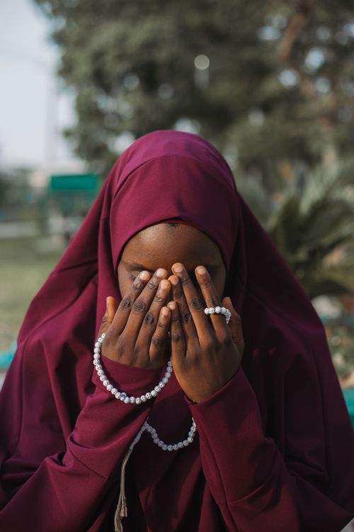 Free A woman in a maroon hijab prays outdoors with a white prayer bead necklace. Stock Photo