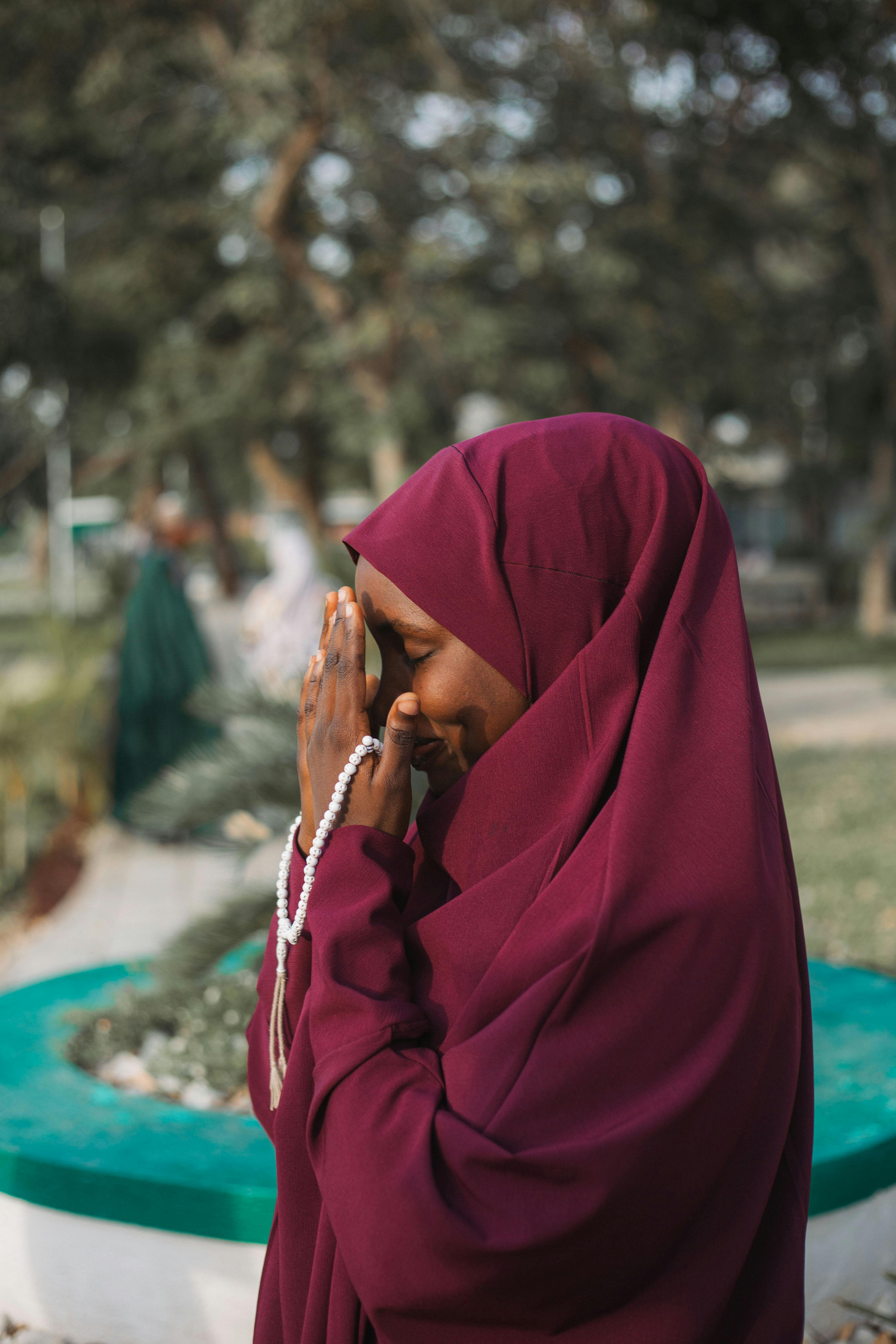 Miễn phí Một người phụ nữ đội khăn trùm đầu màu đỏ tía đang cầu nguyện ngoài trời ở Dubai, thể hiện sự kết hợp giữa tâm linh và thời trang. Ảnh lưu trữ