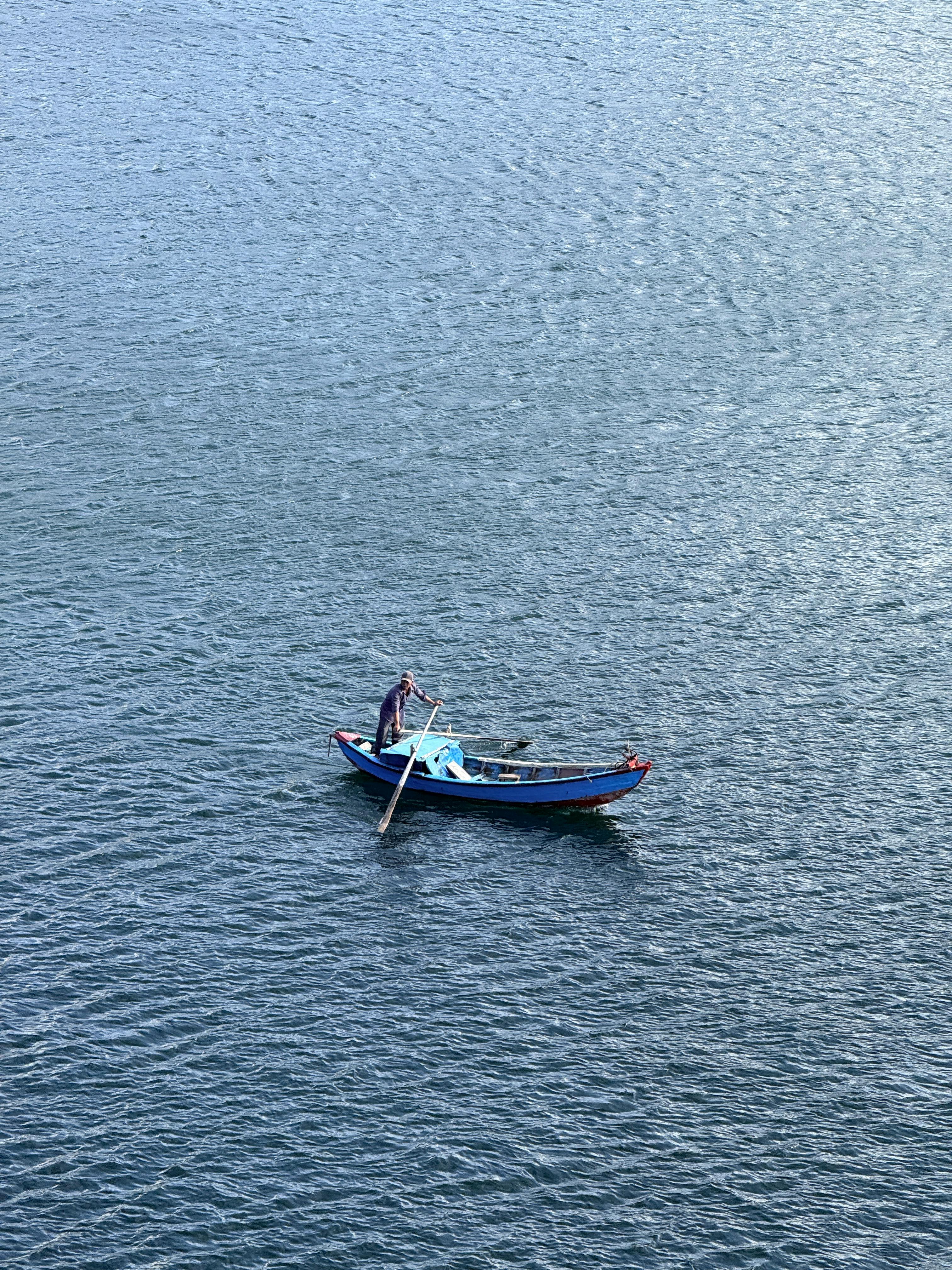 grátis Um pescador solitário rema seu barco pelas águas calmas e extensas da Baía de Nha Trang, no Vietnã. Foto profissional