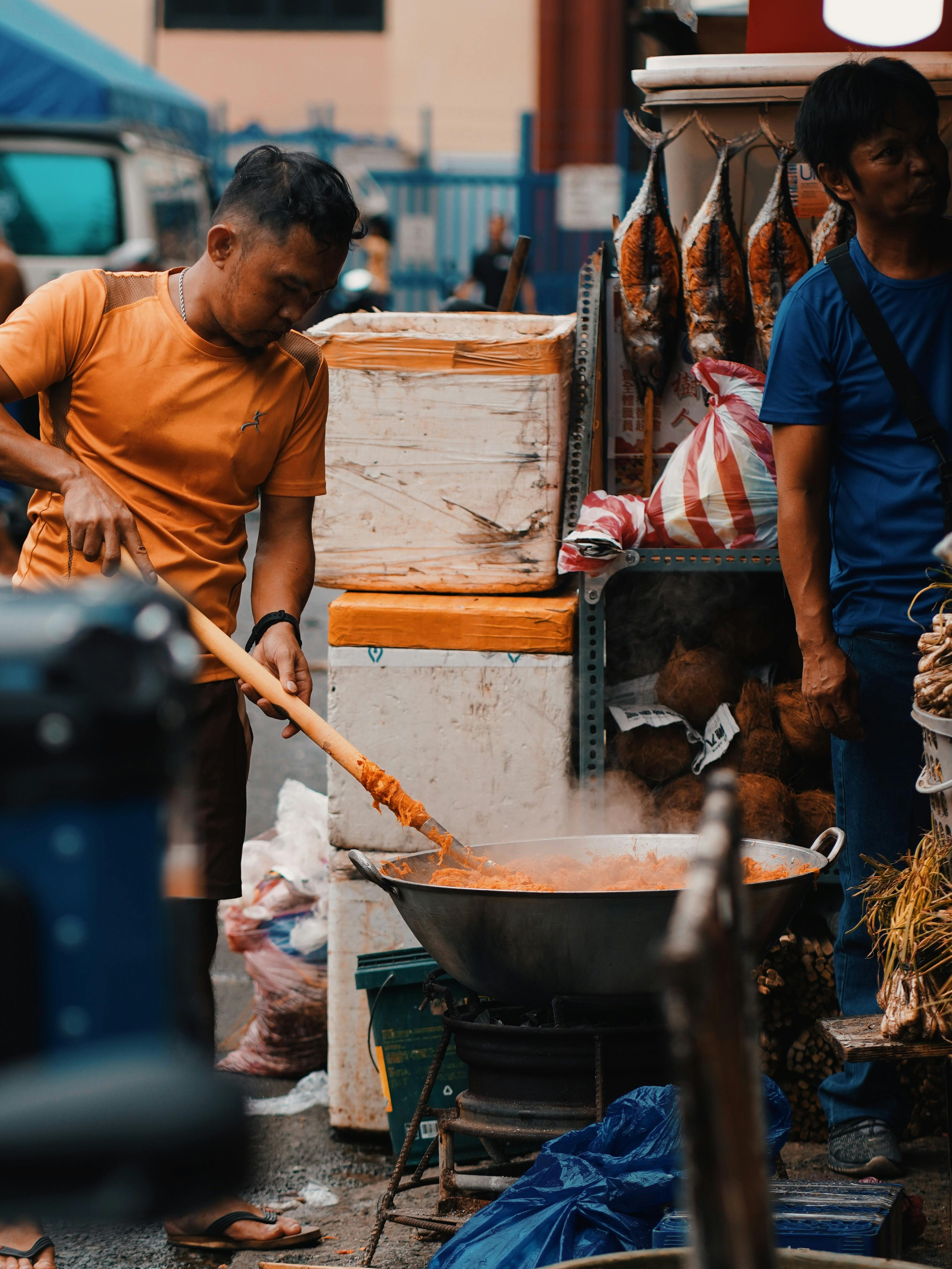Street vendor cooking stir fry in large wok at bustling outdoor market.