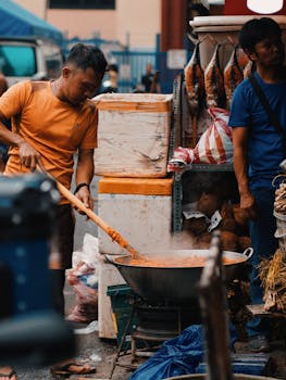Street vendor cooking stir fry in large wok at bustling outdoor market.