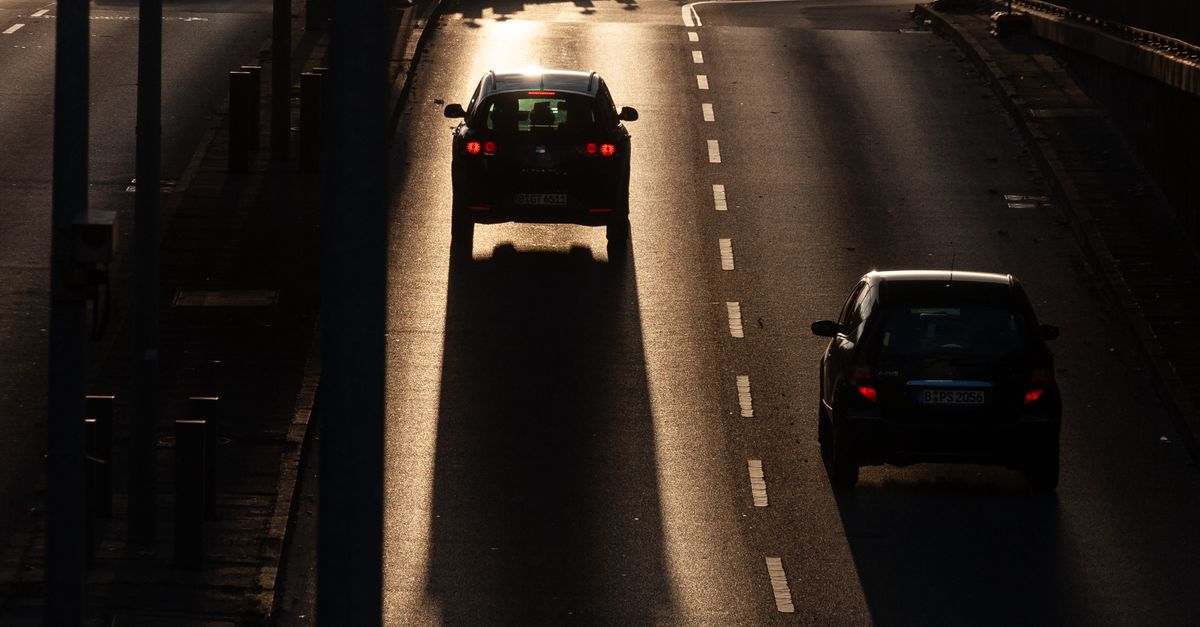 Dramatic twilight scene of cars driving on a city highway, casting long shadows.