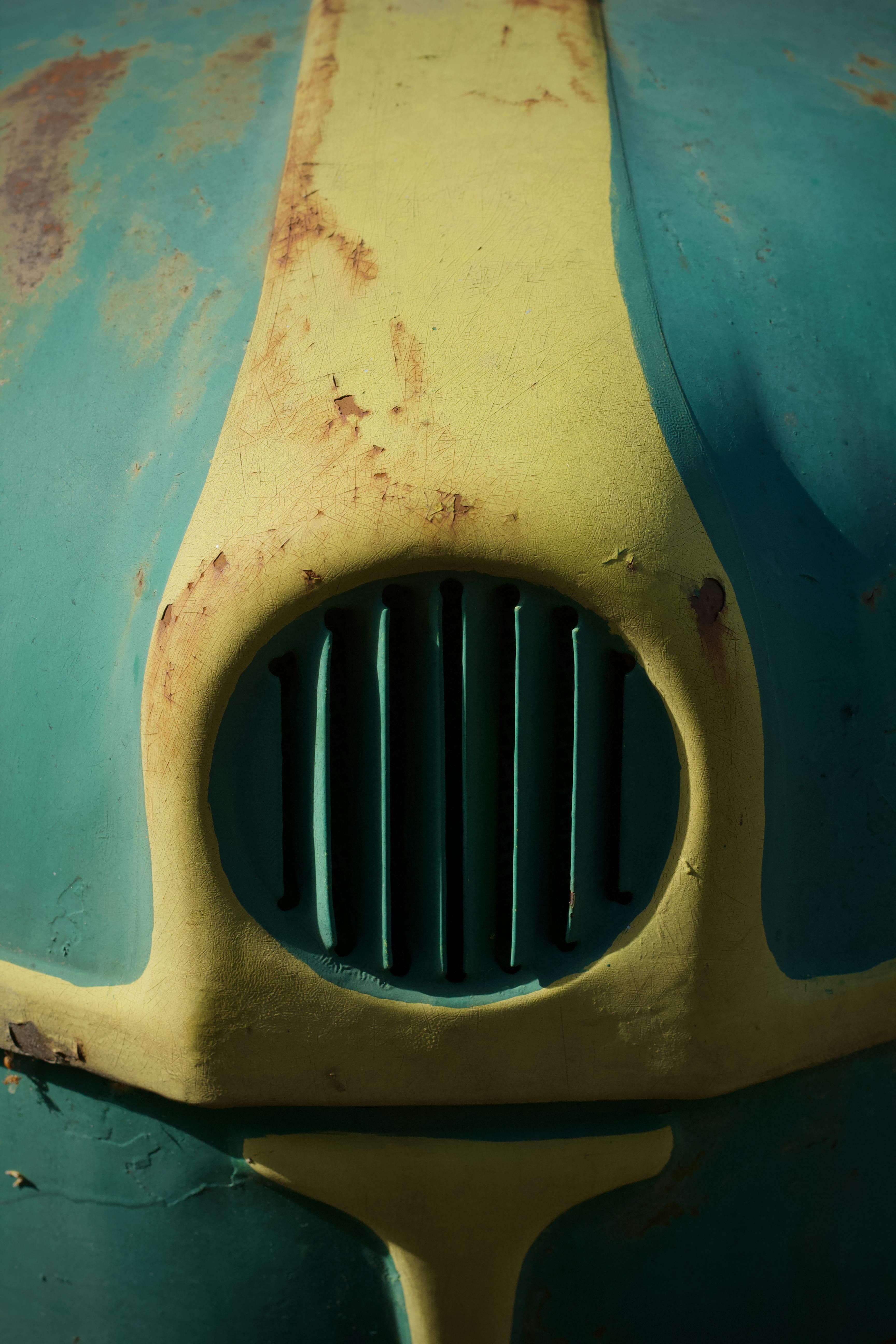 Free Close-up of a classic car hood showcasing rustic teal and yellow paintwork with signs of aging. Stock Photo
