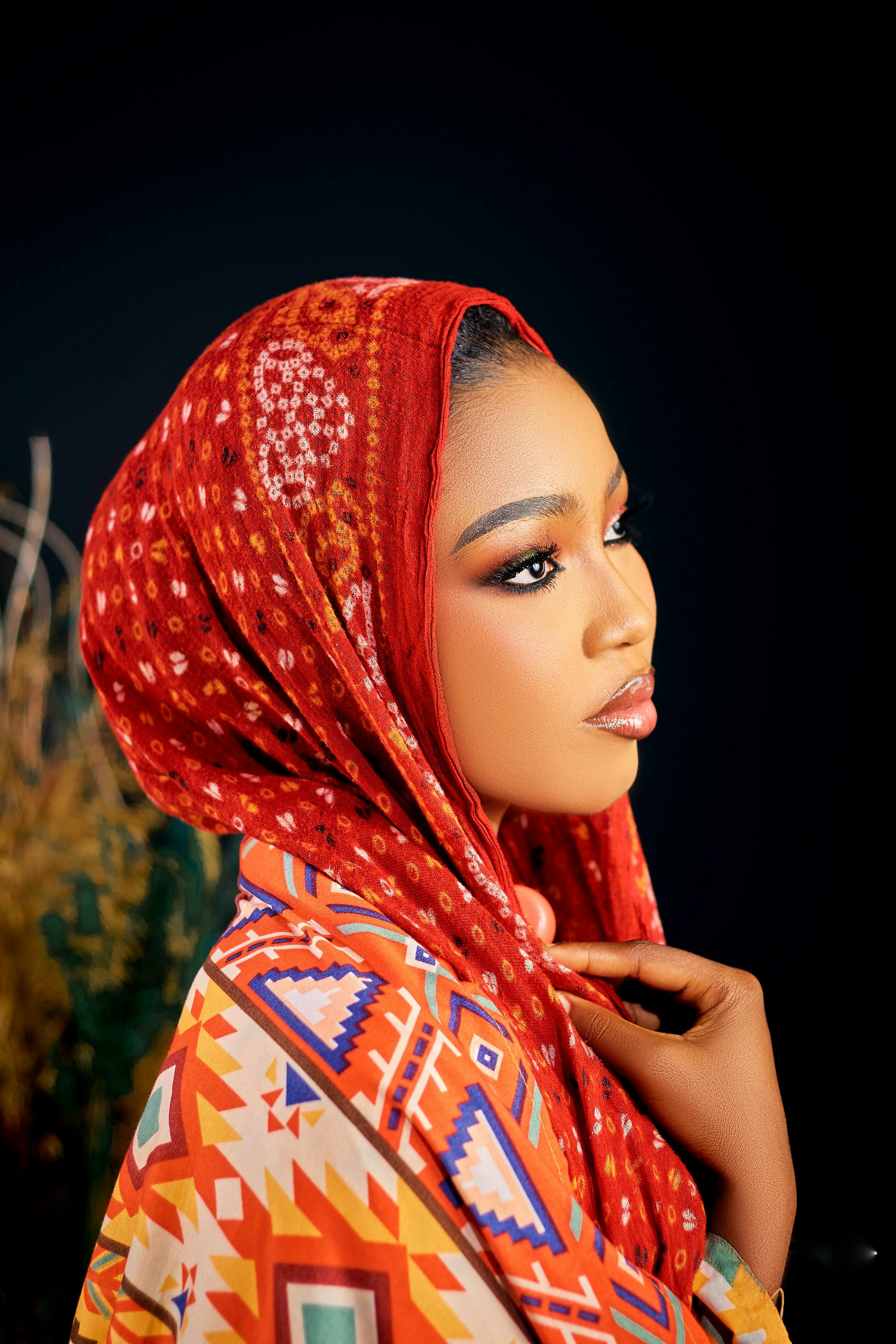Side portrait of a woman in a vibrant patterned hijab against a dark background.