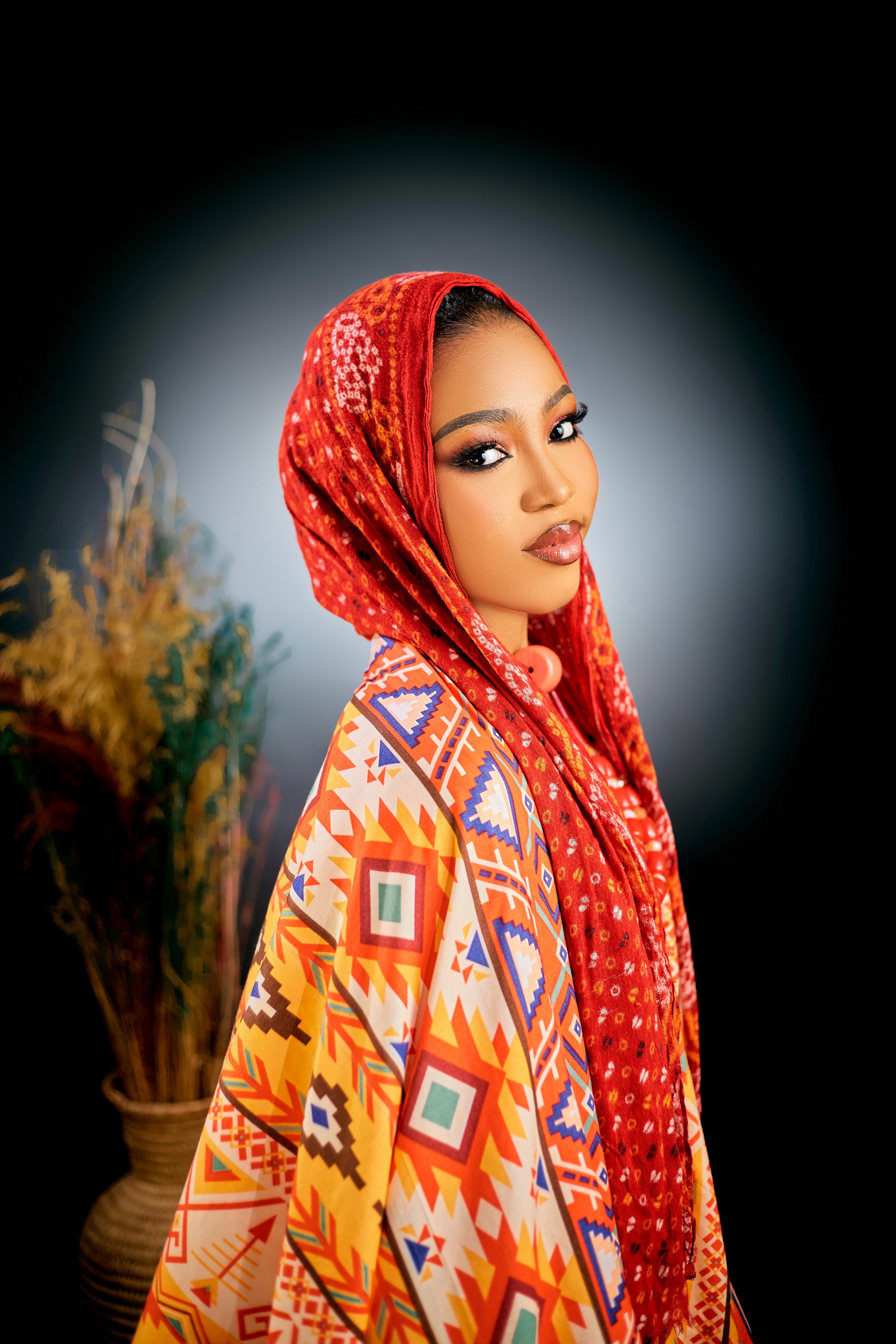 Captivating portrait of a woman wearing colorful, geometric-patterned attire and a red headscarf.