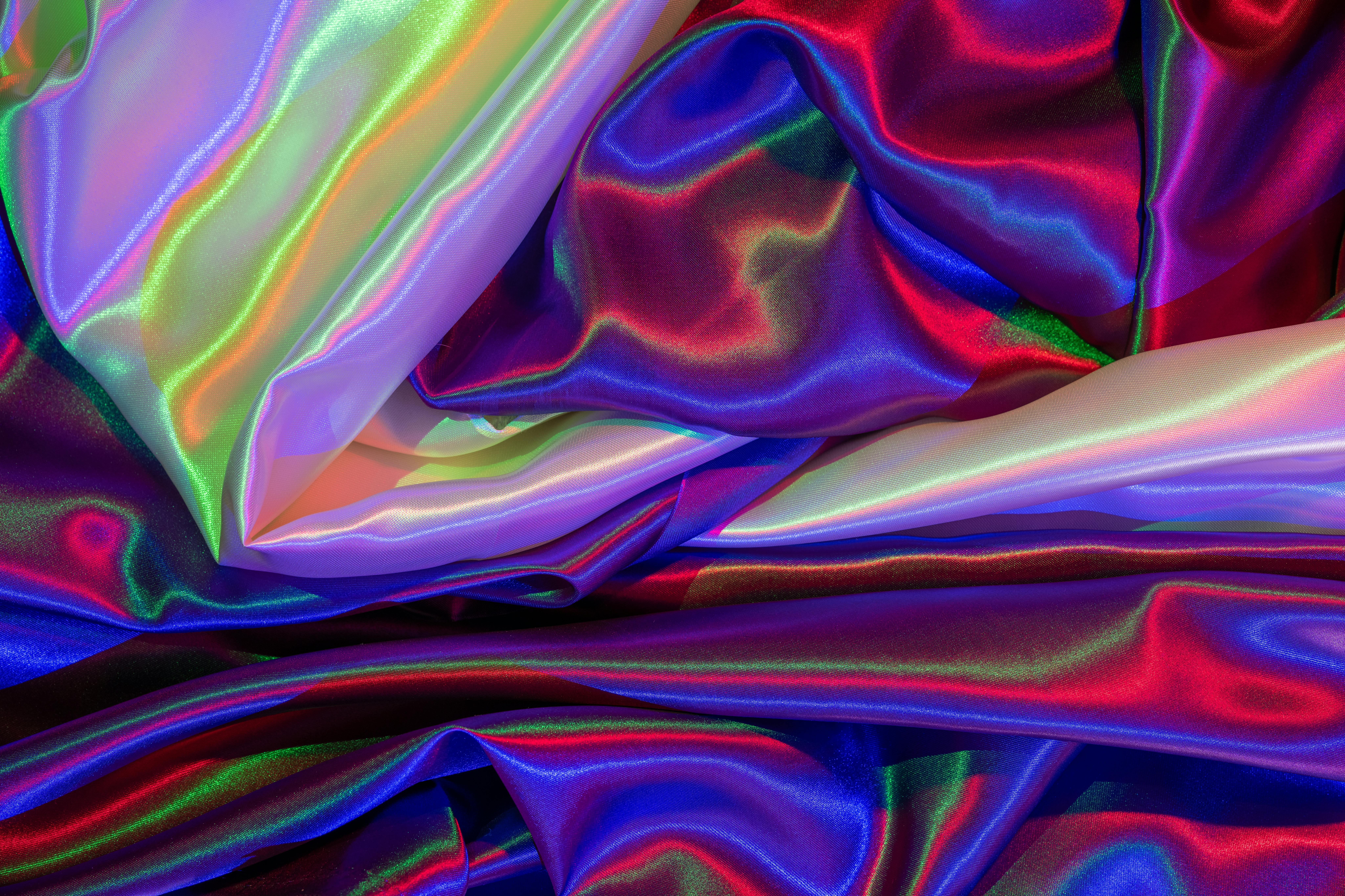 Free A close-up of vibrant satin fabric displaying colorful ripples and folds in a dynamic abstract pattern. Stock Photo