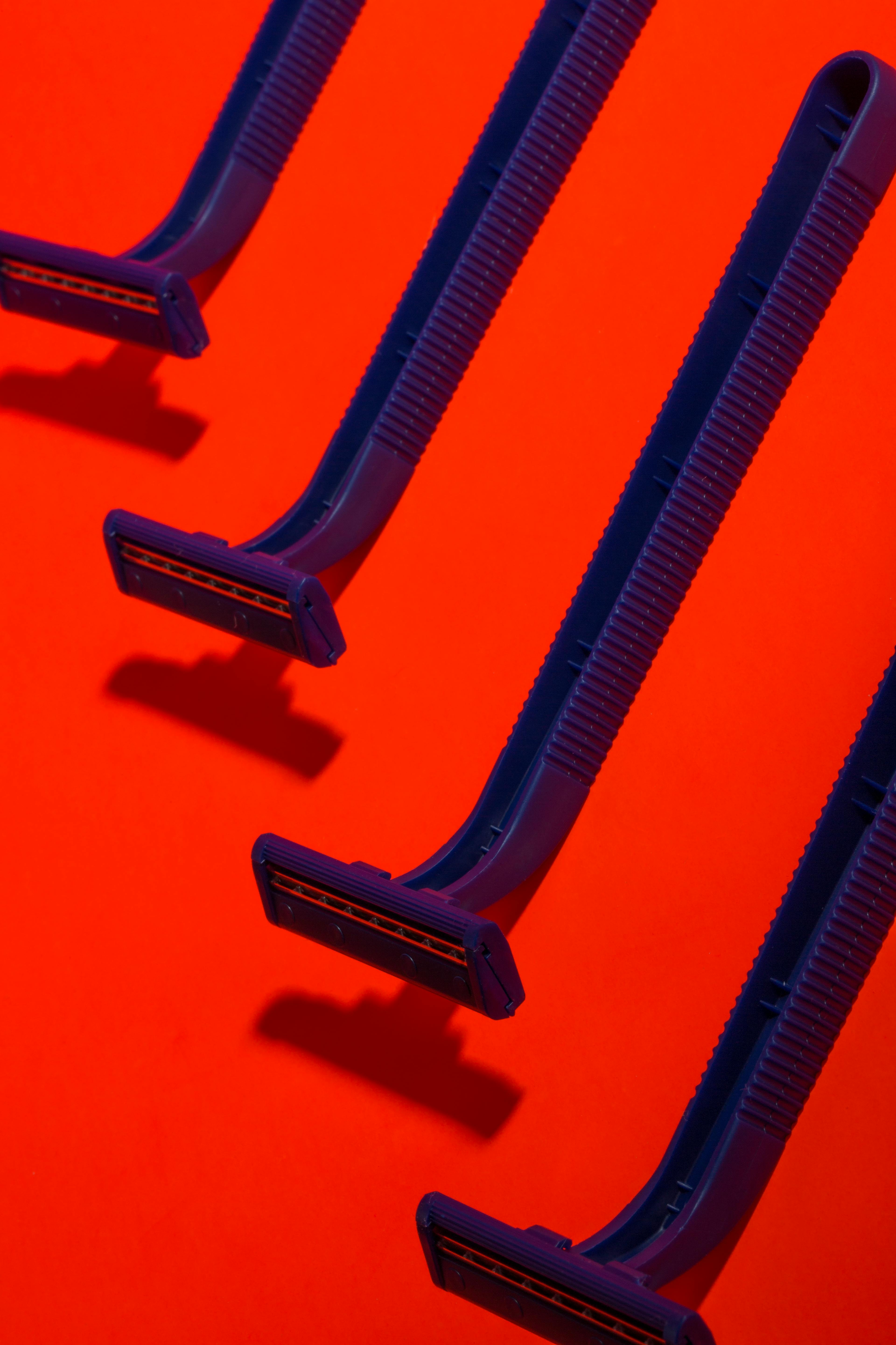 Gratis Fire blå engangsbarberblade kunstnerisk arrangeret på en livlig rød baggrund. Lagerfoto