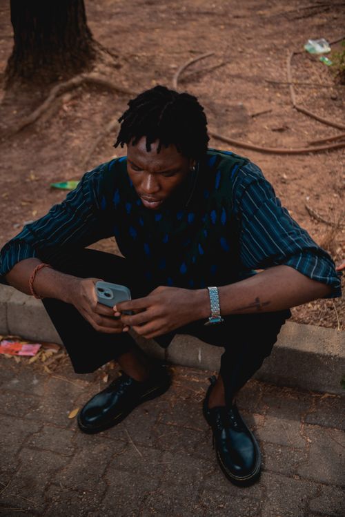 Free Young man in casual attire sitting on a curb outside, engaging with his smartphone. Stock Photo