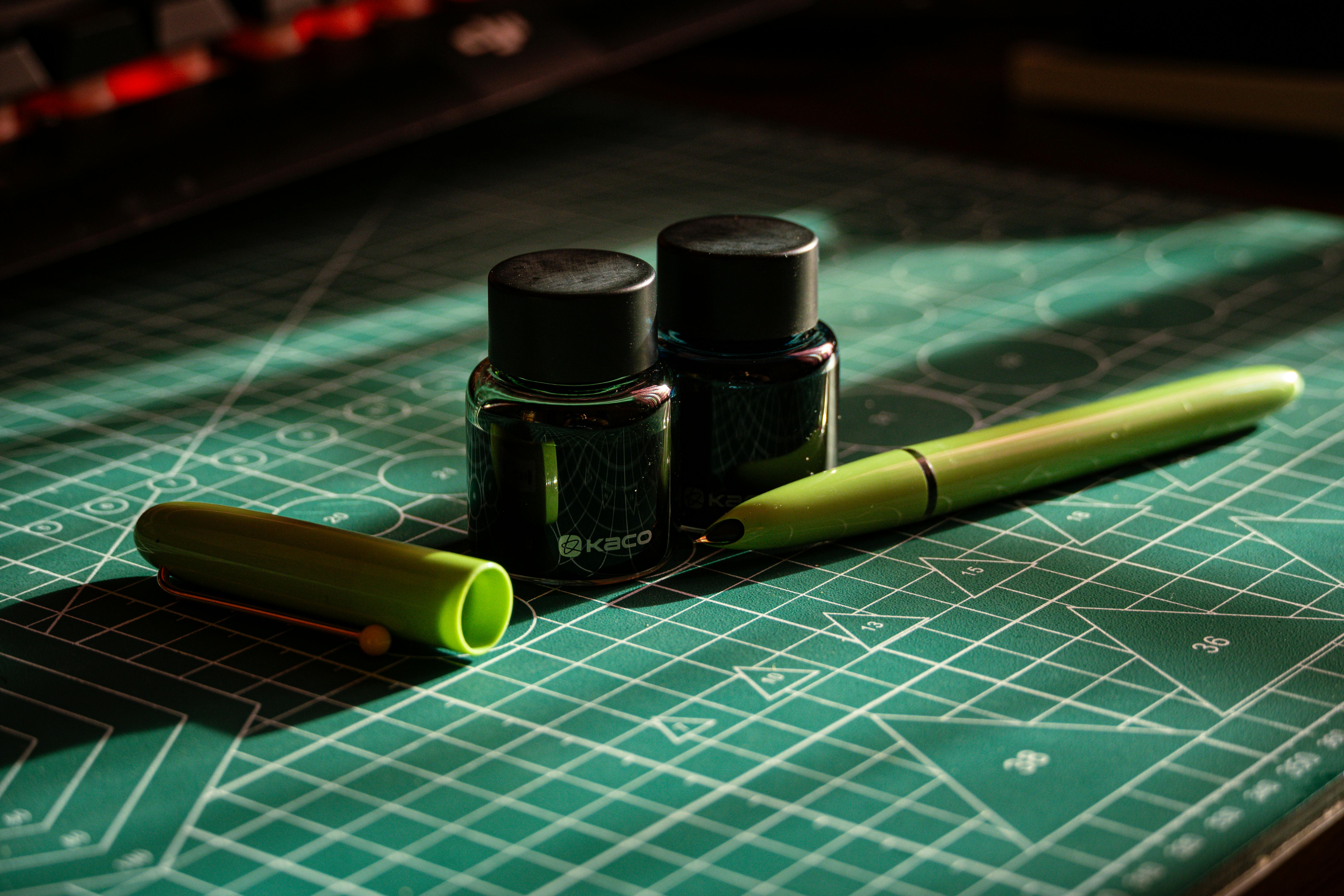 bezplatná Zelené pero a dvě lahvičky s inkoustem na řezací podložce v uměleckém aranžmá. Základová fotografie
