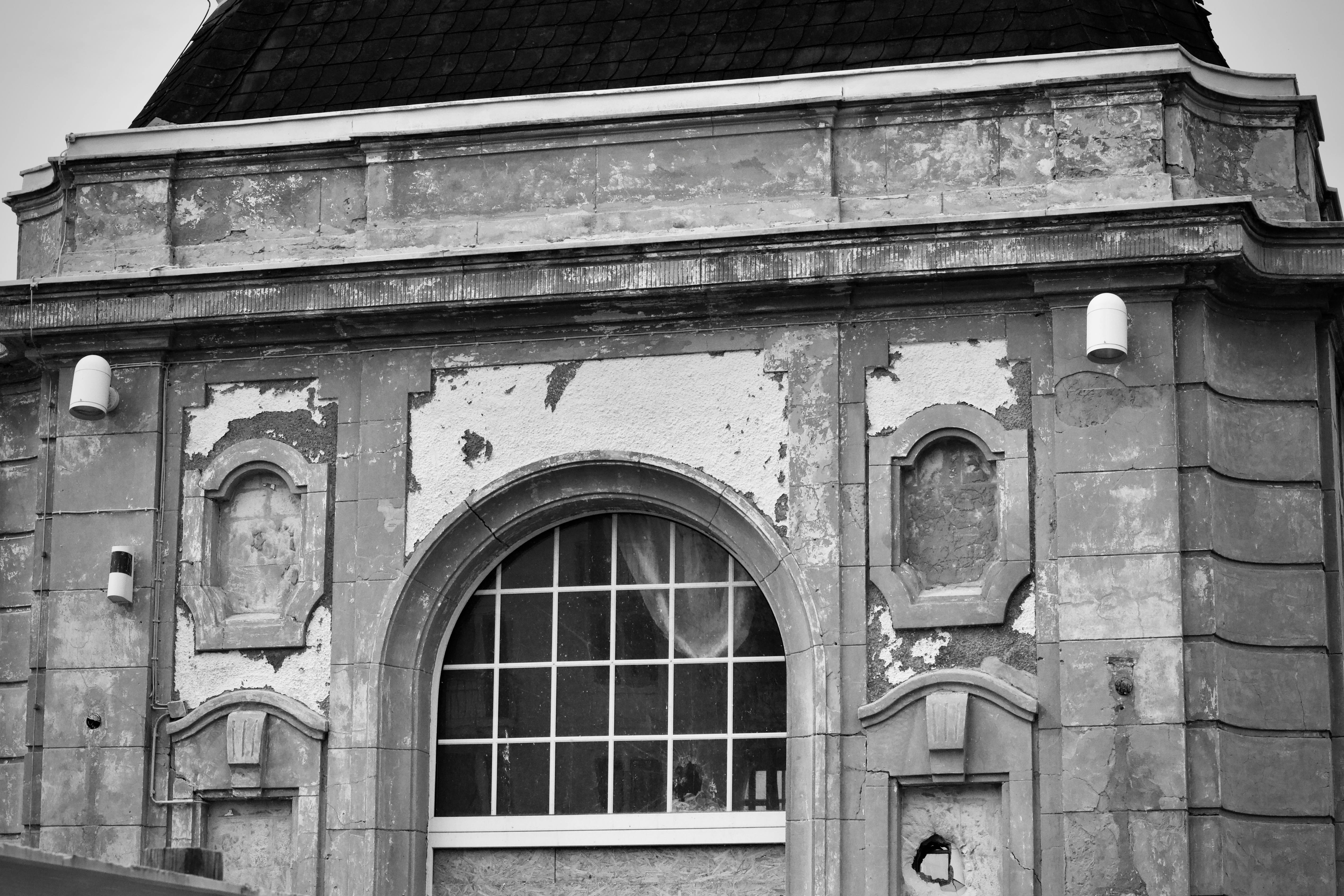 Gratis Sort-hvidt billede, der foreviger en gammel, vejrbidt stenbygningsfacade med buet vindue. Lagerfoto