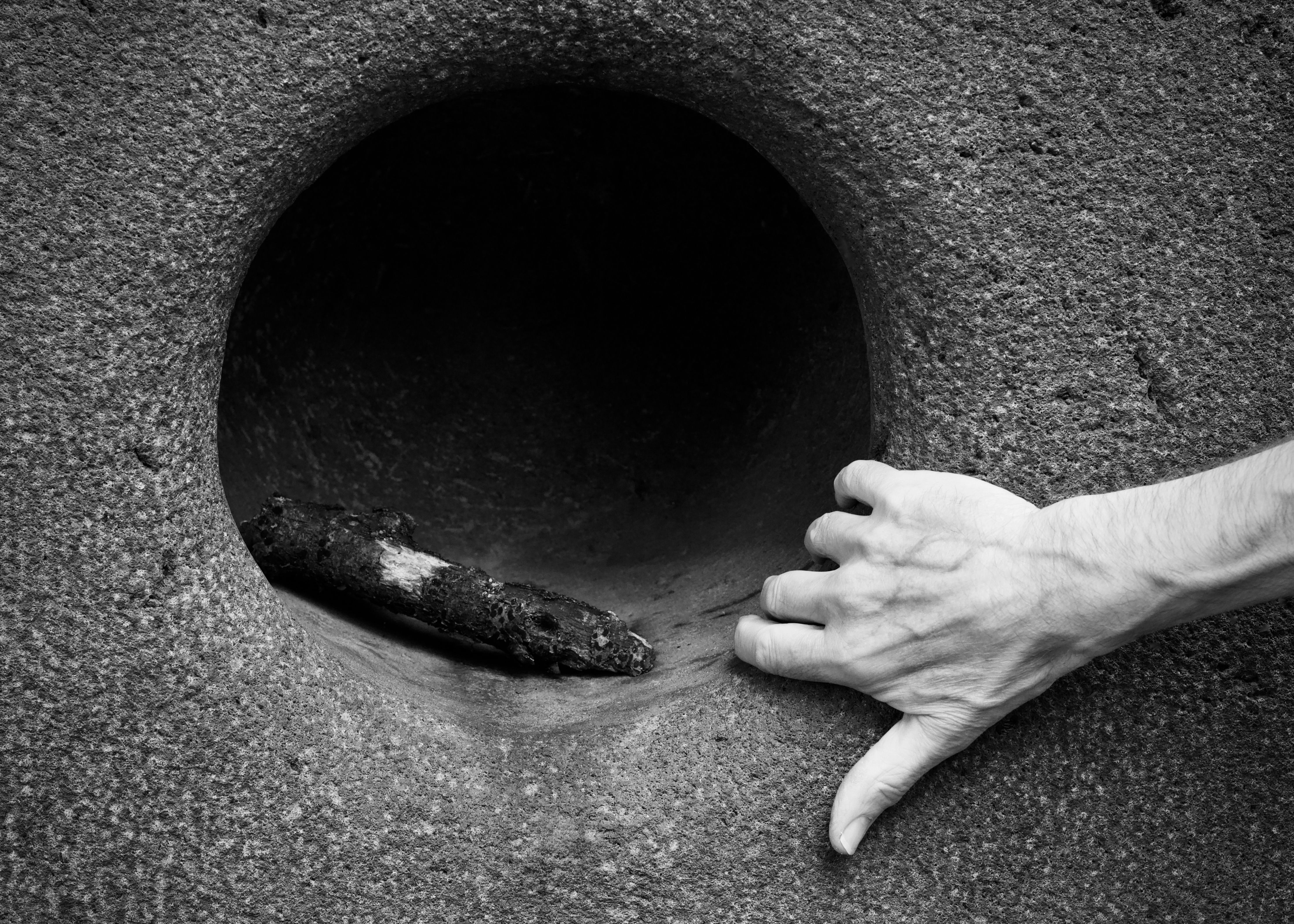 Close-up black and white image of a hand interacting with a stone sculpture, emphasizing texture.