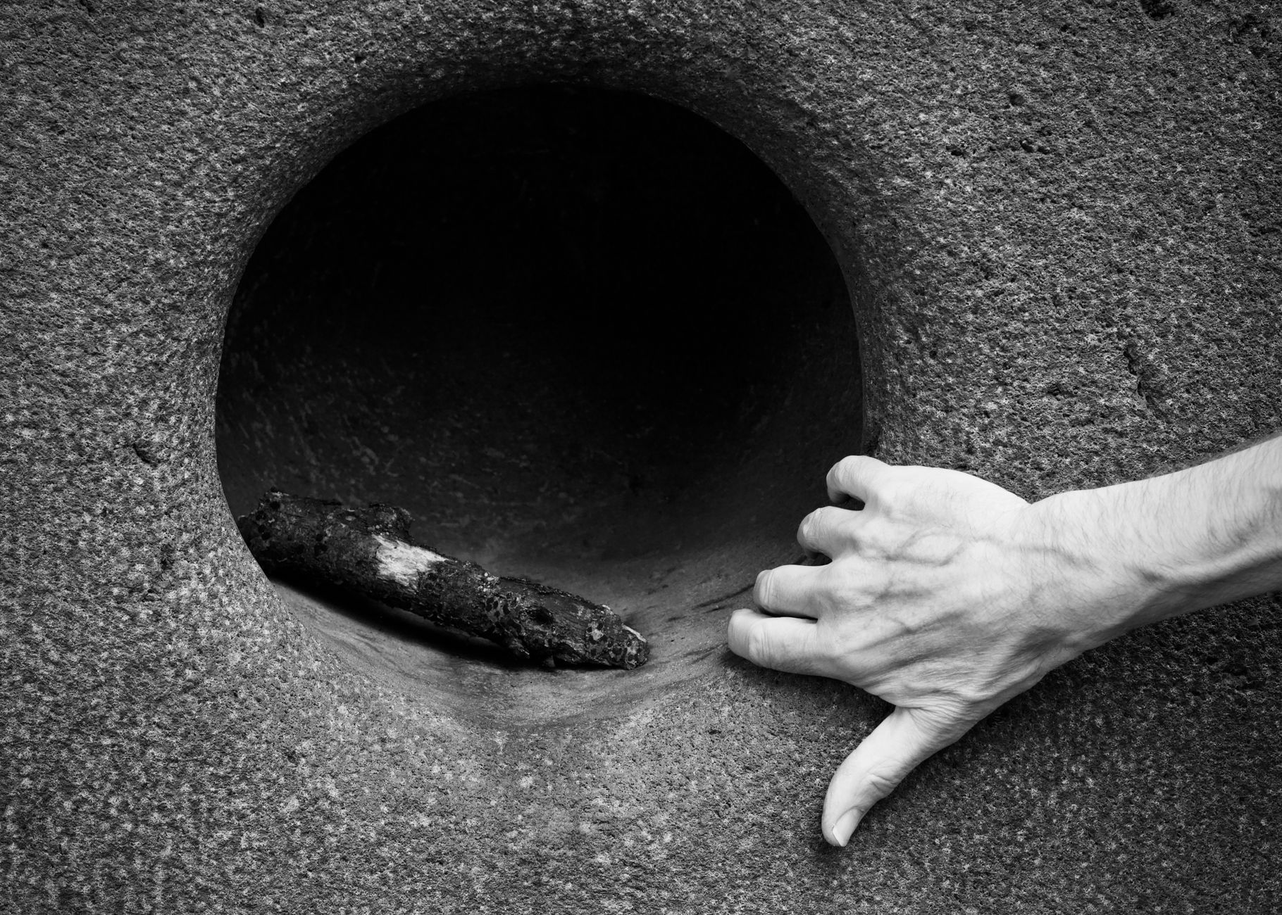 Close-up black and white image of a hand interacting with a stone sculpture, emphasizing texture.