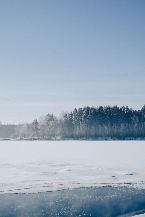 Free A tranquil snowy landscape featuring a frozen lake and evergreen forest under a clear blue sky. Stock Photo