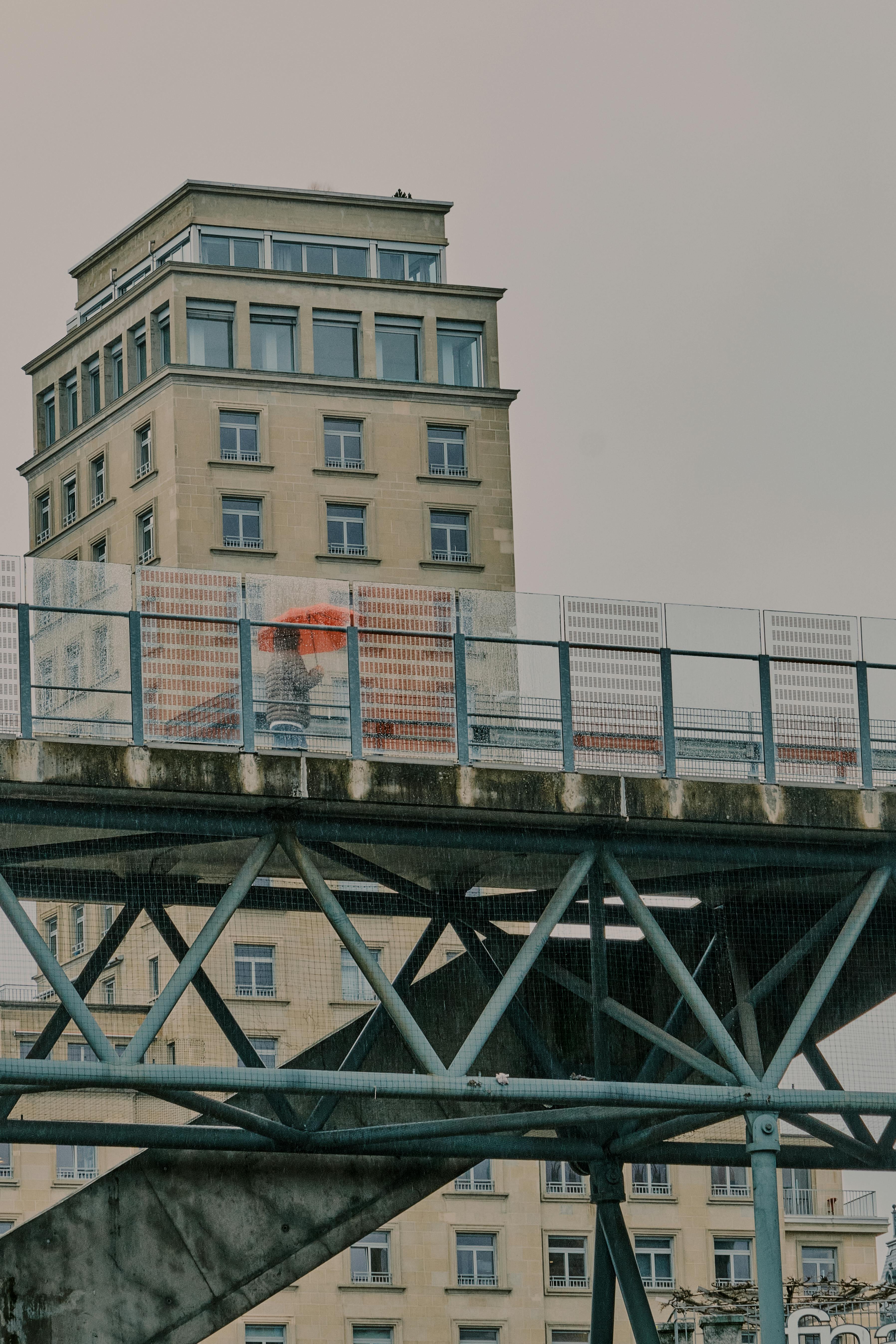 Free A captivating urban scene in Lausanne featuring a person with a red umbrella on a footbridge. Stock Photo