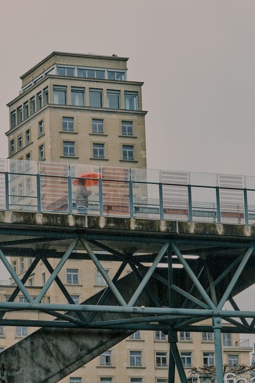 Free A captivating urban scene in Lausanne featuring a person with a red umbrella on a footbridge. Stock Photo