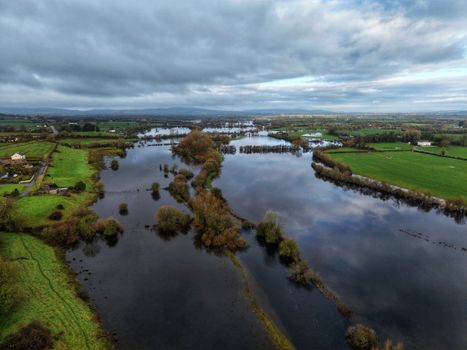 Aerial shot of rural landscape with flooded fields under cloudy sky, showcasing nature's beauty.