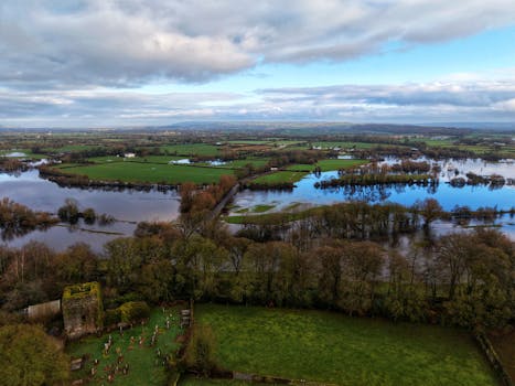 Photo by Jay's Photography A serene aerial view capturing a flooded countryside with trees and farmlands under a cloudy sky.