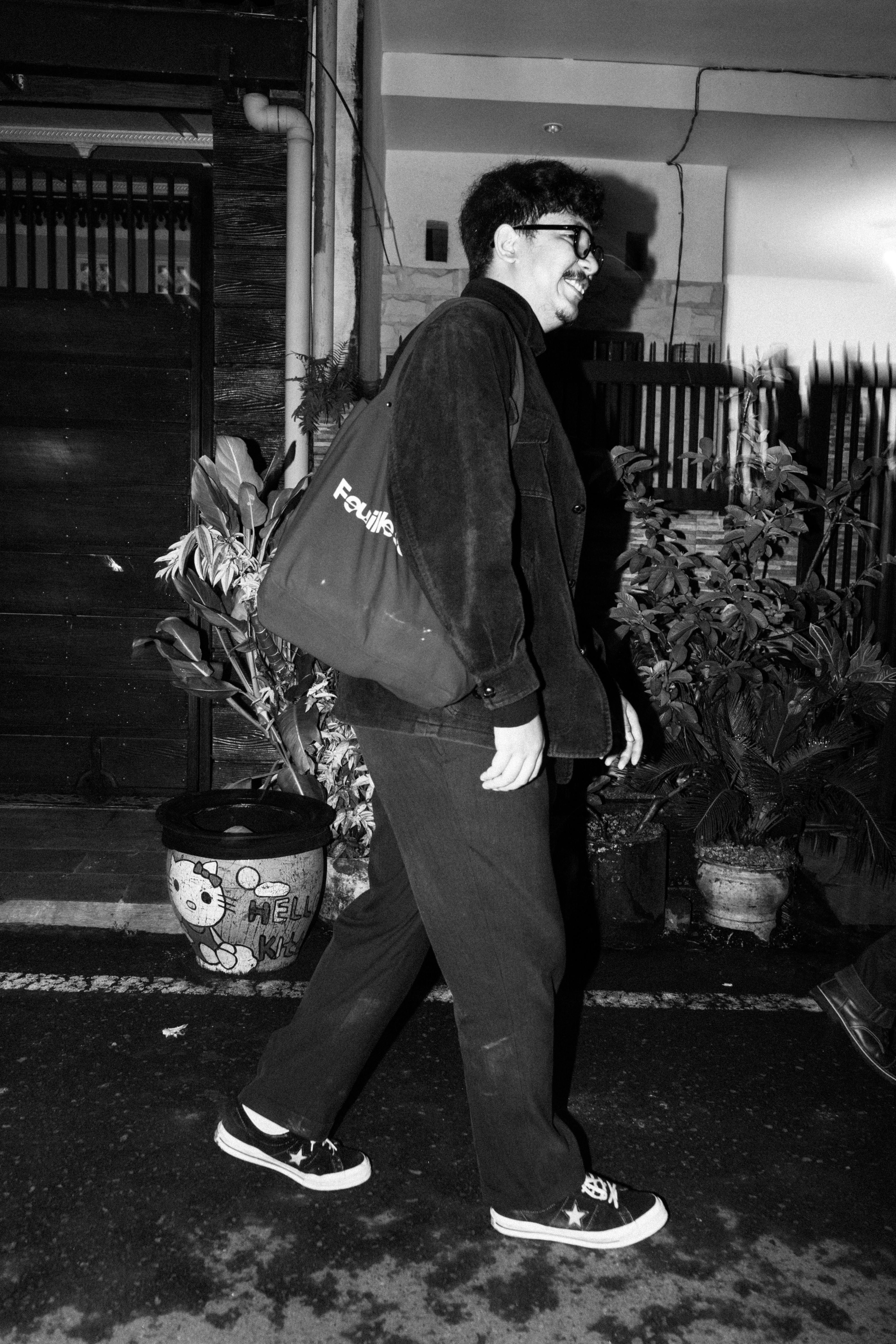 Black and white photo of a man walking on a street at night, smiling.