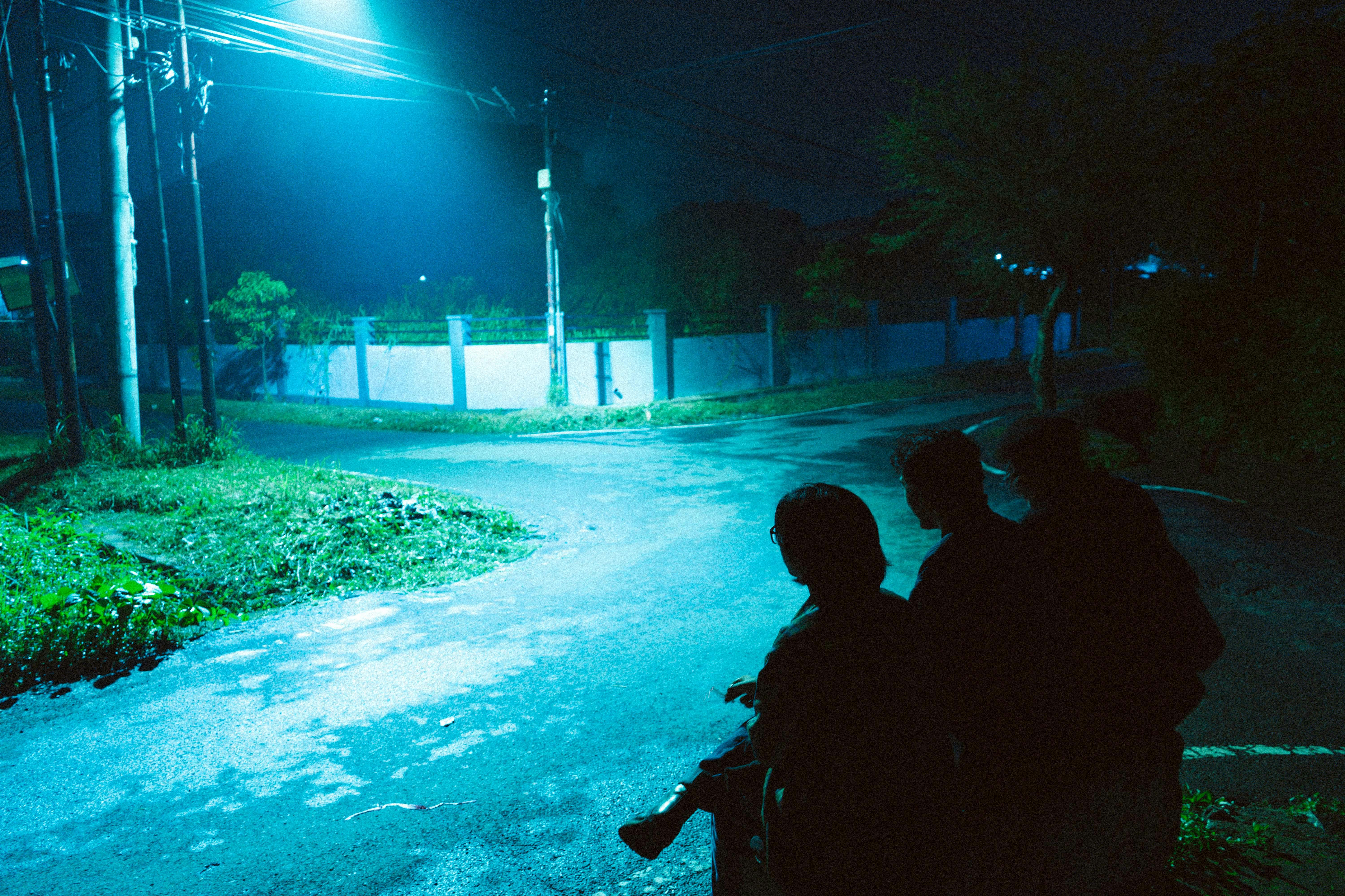 Ücretsiz Gece vakti, ıssız bir sokak köşesinde, sokak lambasının altında insanların siluetleri. Stok Fotoğraflar