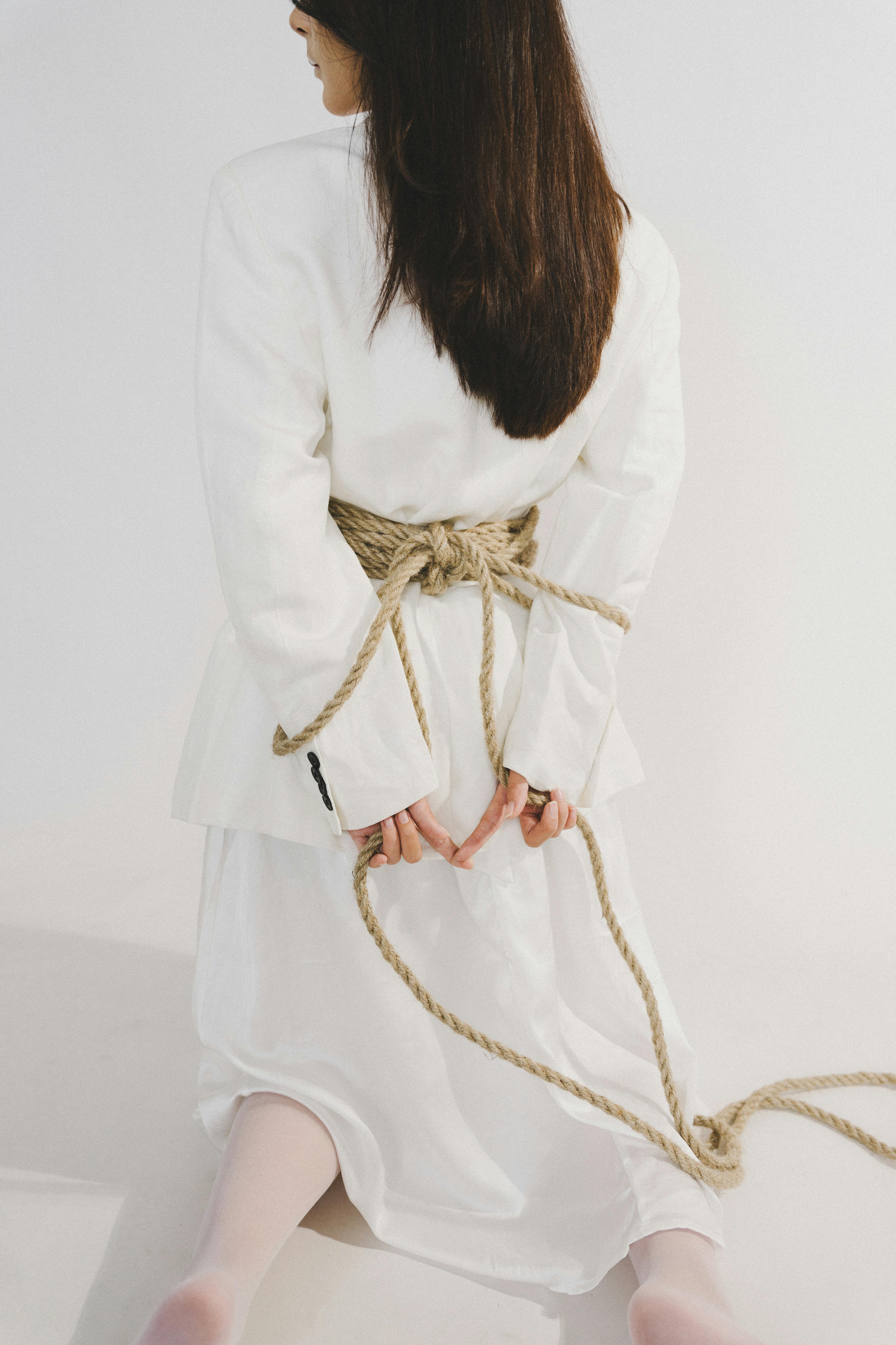Gratis Una mujer con un vestido blanco arrodillada y atada con una cuerda, pose simbólica. Foto de stock
