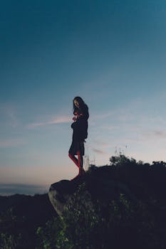 A solitary figure stands on a hill at dusk, creating a moody atmosphere against a twilight sky.
