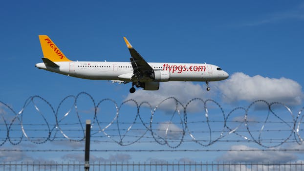 A Pegasus Airlines jet airliner approaches landing over barbed wire fence against blue sky.